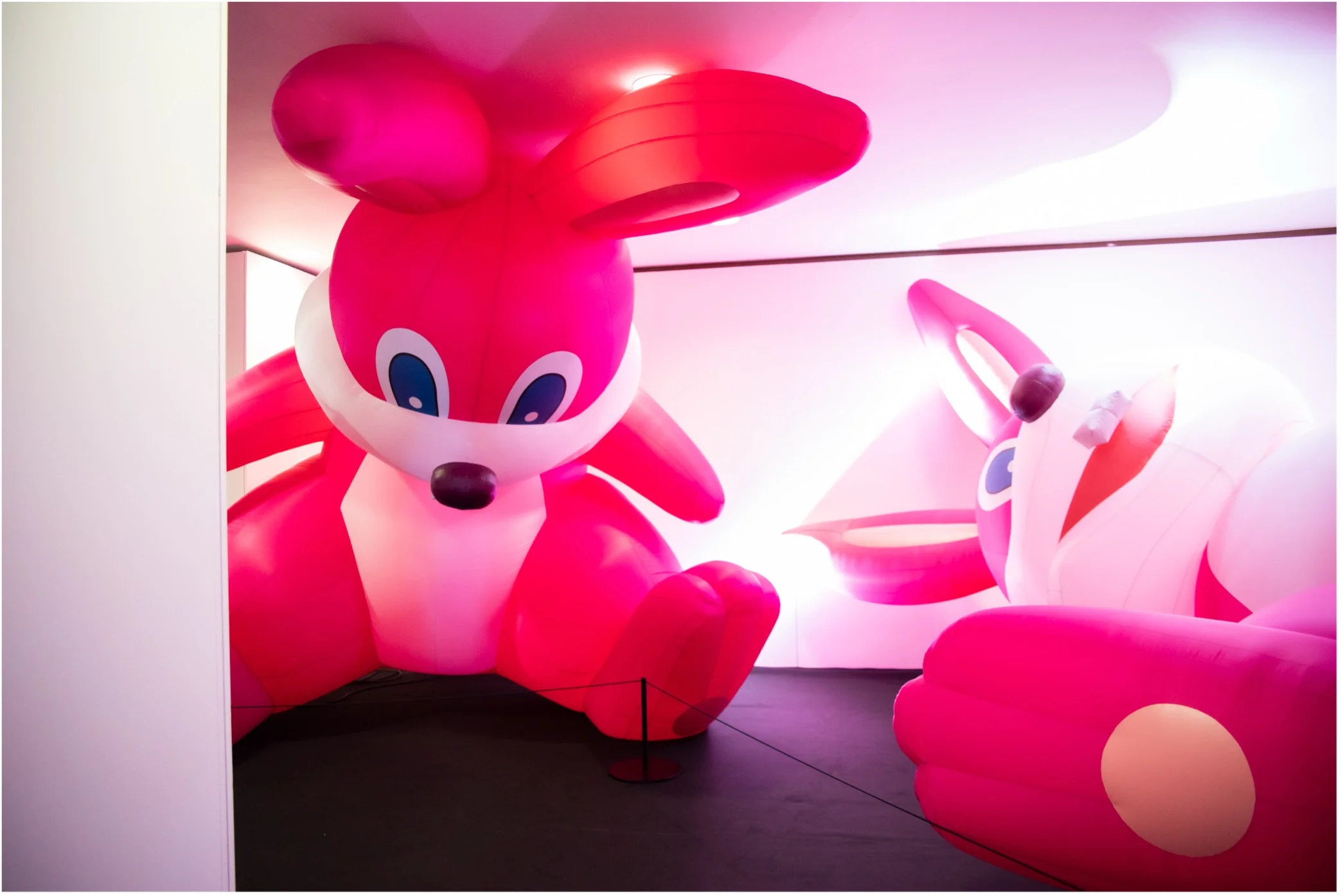 Large pink inflatable bunnies filling a tight white room, from Somehow I Dont Feel Comfortable by Momoyo Torimitsu at Balloon Museum.