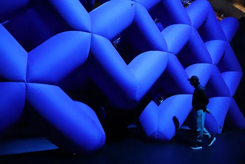 Visitor walking beside a large blue geometric inflatable tunnel from Cube Abyss by Cyril Lancelin at Balloon Museum.