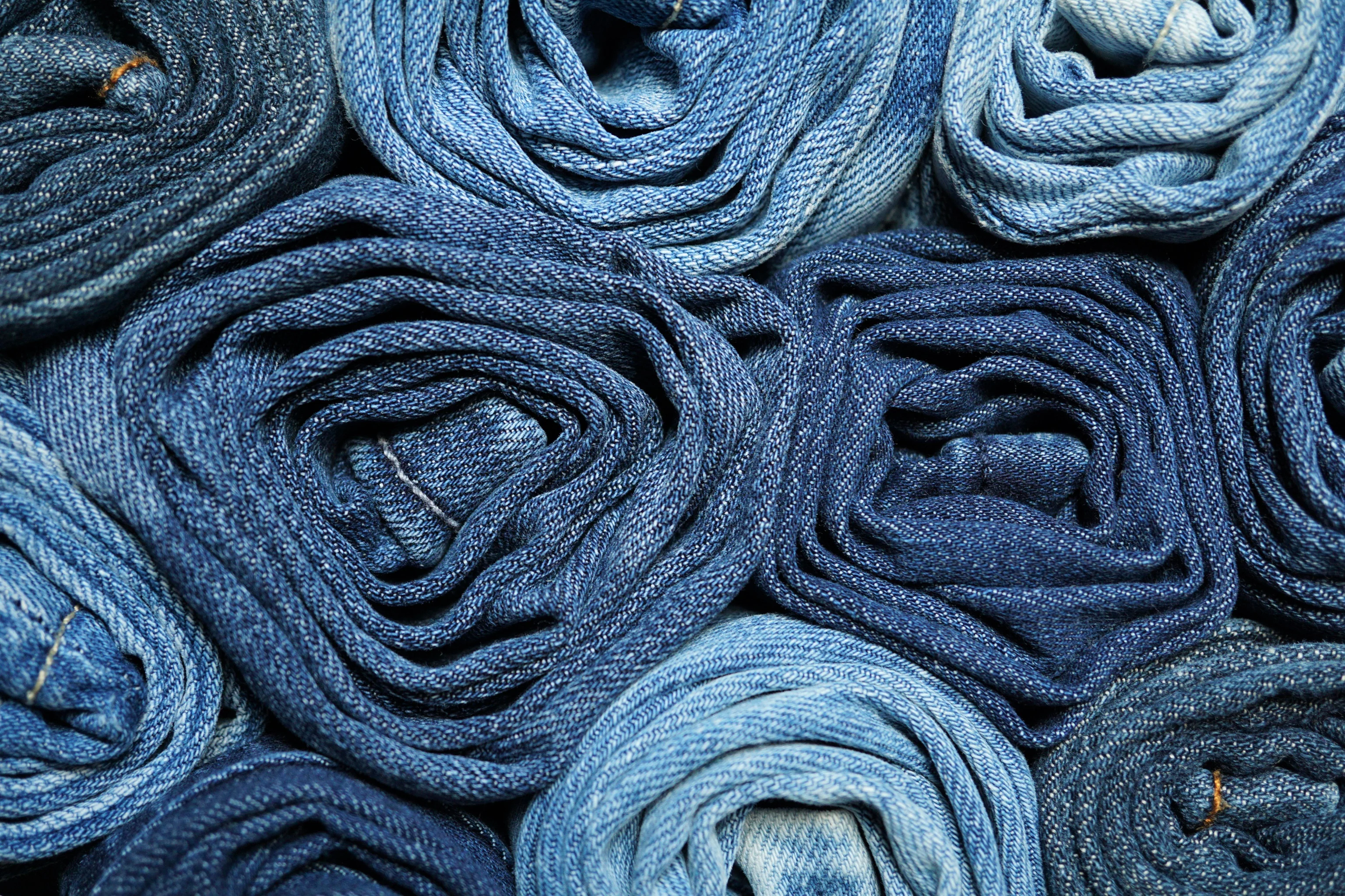 Close-up of rolled blue denim fabrics in different shades, suggesting recycled or upcycled jeans.