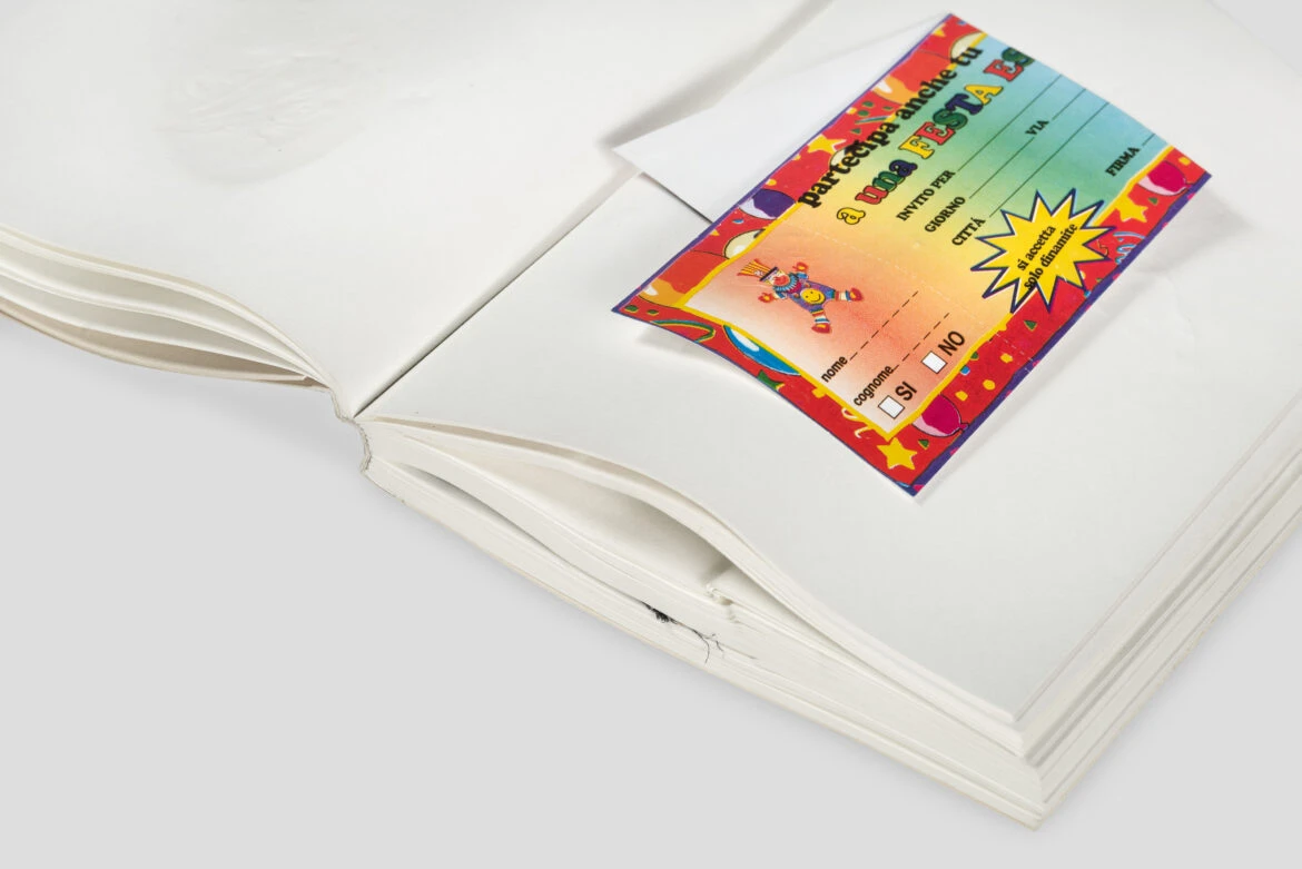 Open artist book with a colorful Italian party invitation card inserted between white pages from Daniel Knorrs LIBER ARTIFICIS, published by NERO.