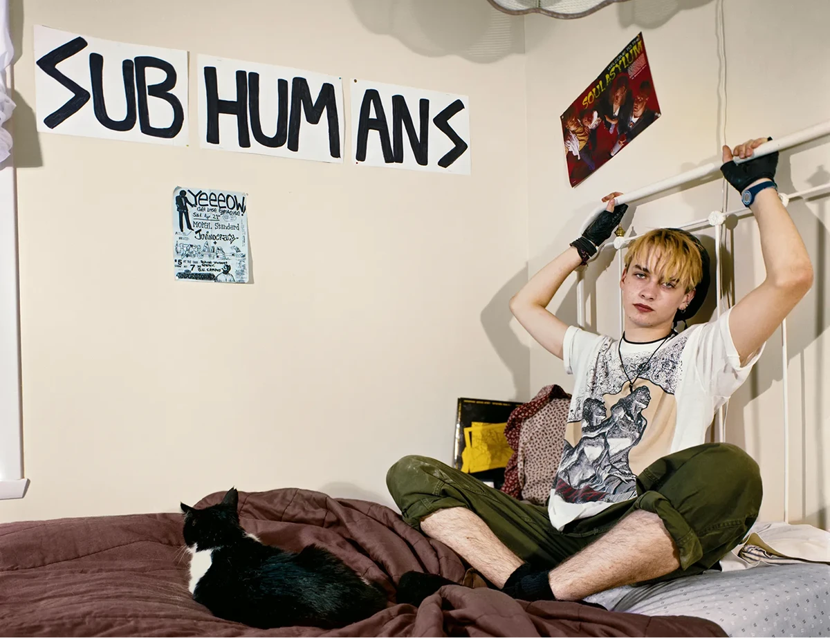 Teenage boy sitting cross-legged on his bed beneath handwritten wall signs, photographed by Adrienne Salinger in the 1990s.
