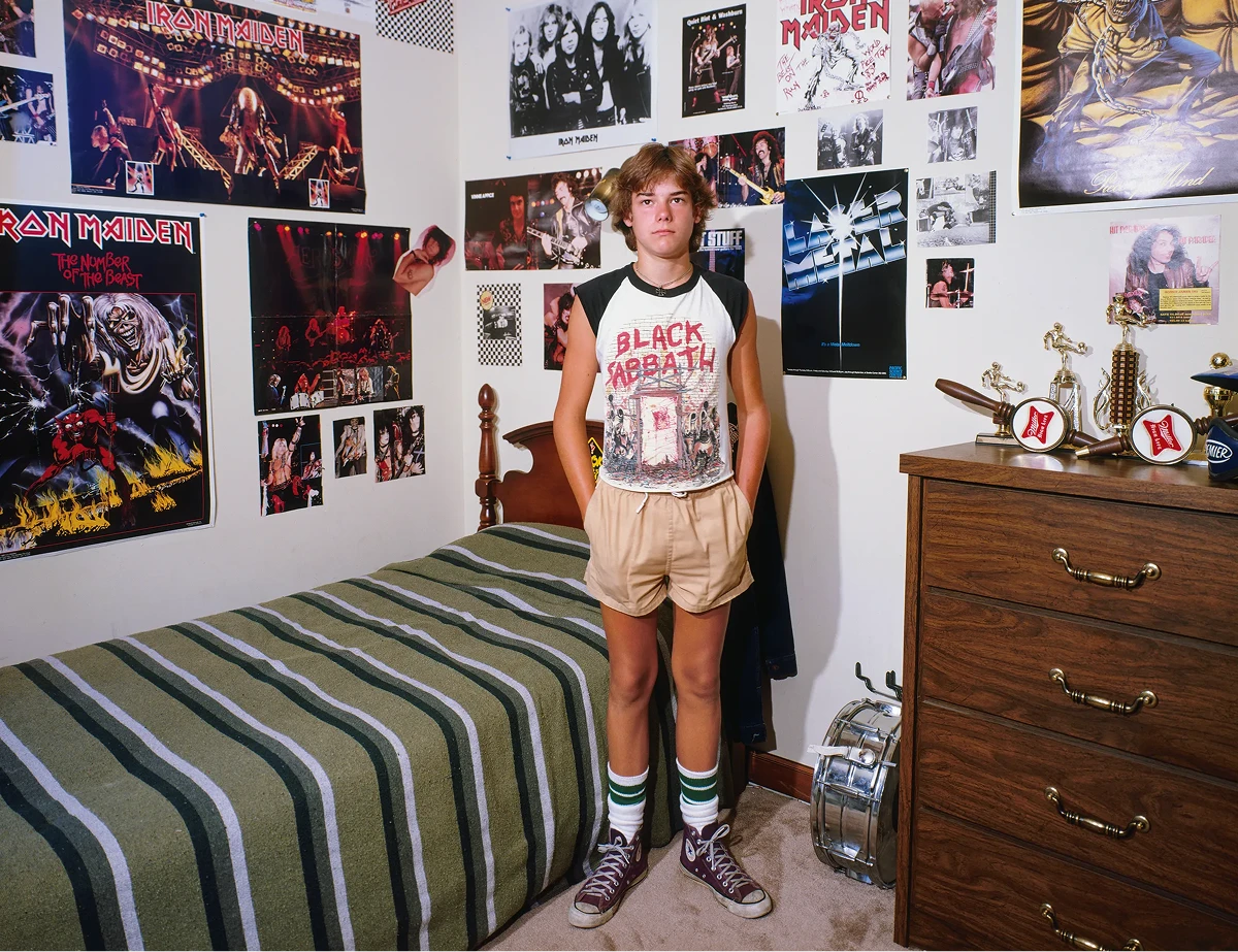 eenage boy standing in her bedroom surrounded by heavy metal band posters, photographed by Adrienne Salinger for the Teenagers in Their Bedrooms series.