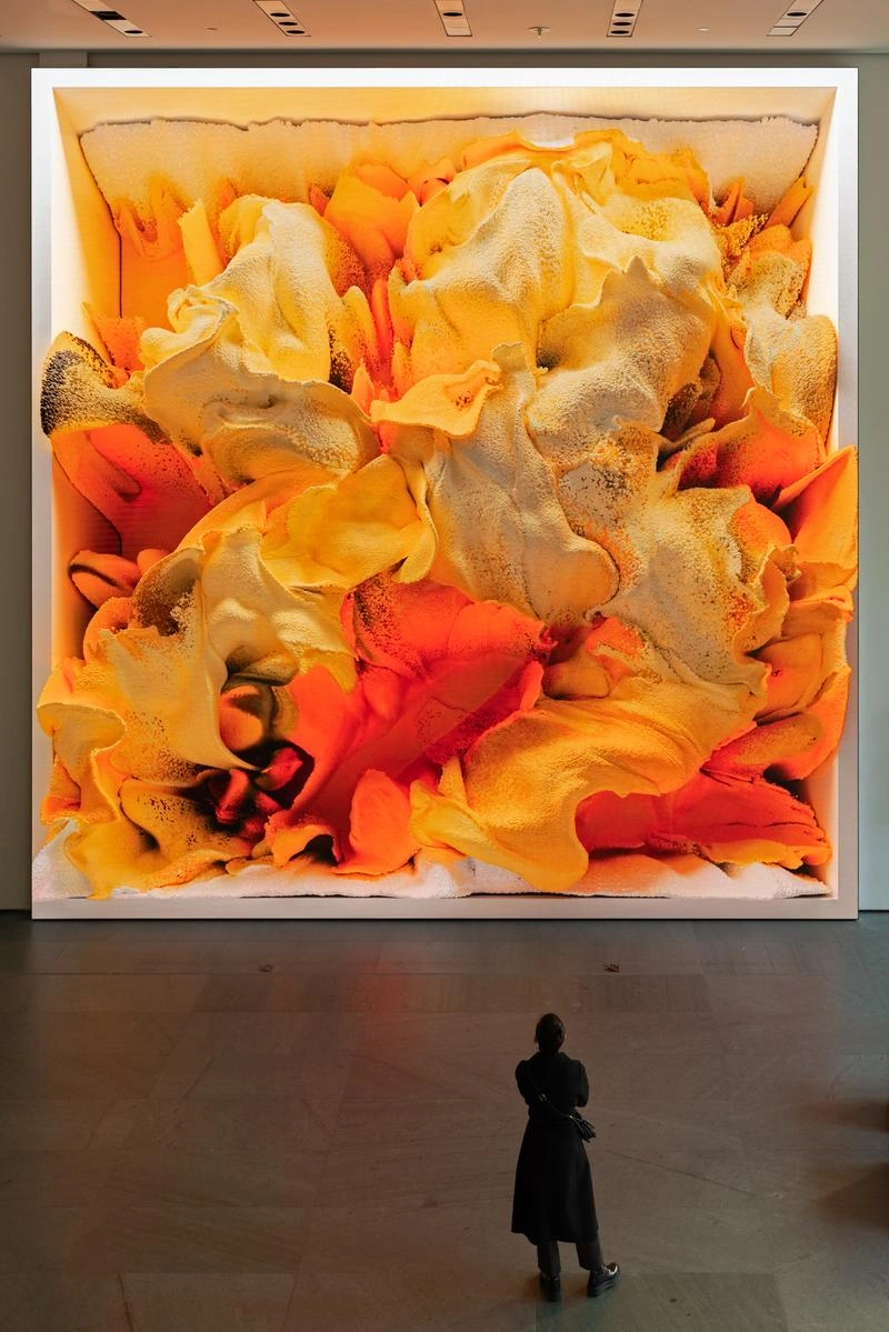Visitor standing in front of a large wall-sized digital artwork with swirling orange and yellow abstract forms in a museum gallery.