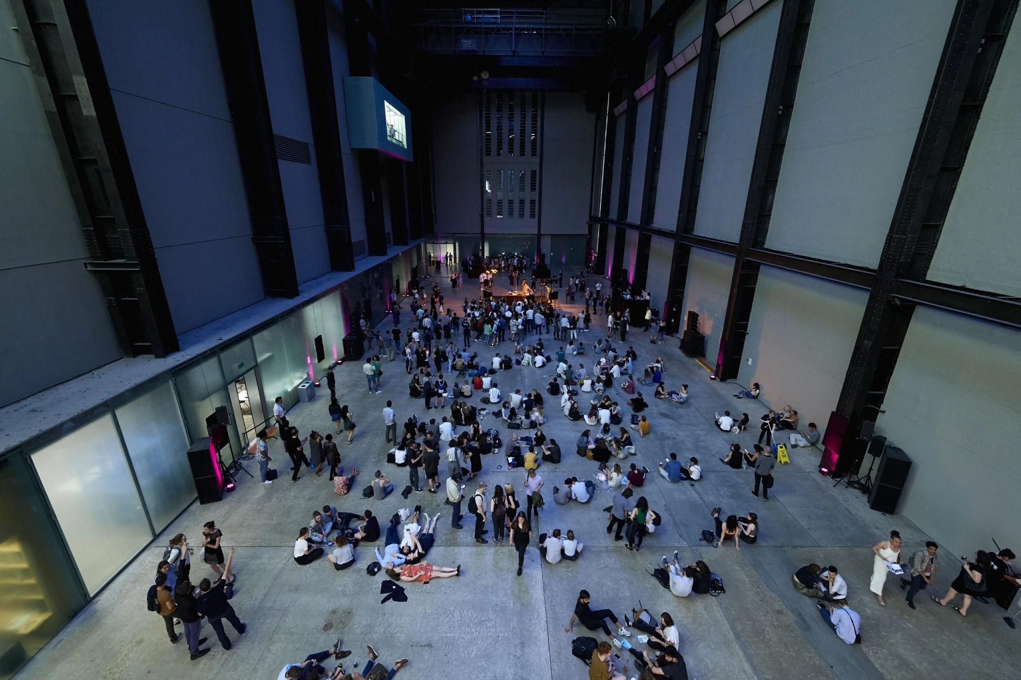 Wide interior view of Tate Modern during a Lates event, showing large groups of visitors gathered inside the Turbine Hall for an evening programme.