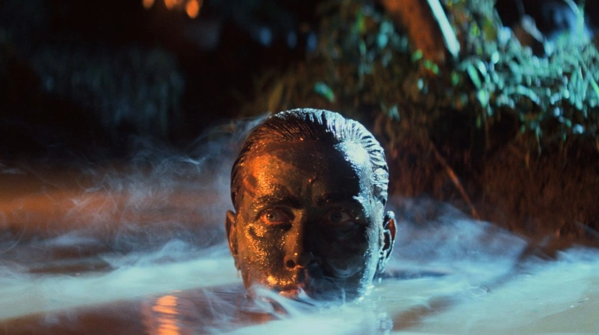 Film still from Apocalypse Now showing Colonel Kurtz emerging from dark water at night, his face partially lit and surrounded by mist, creating a tense and ominous atmosphere.