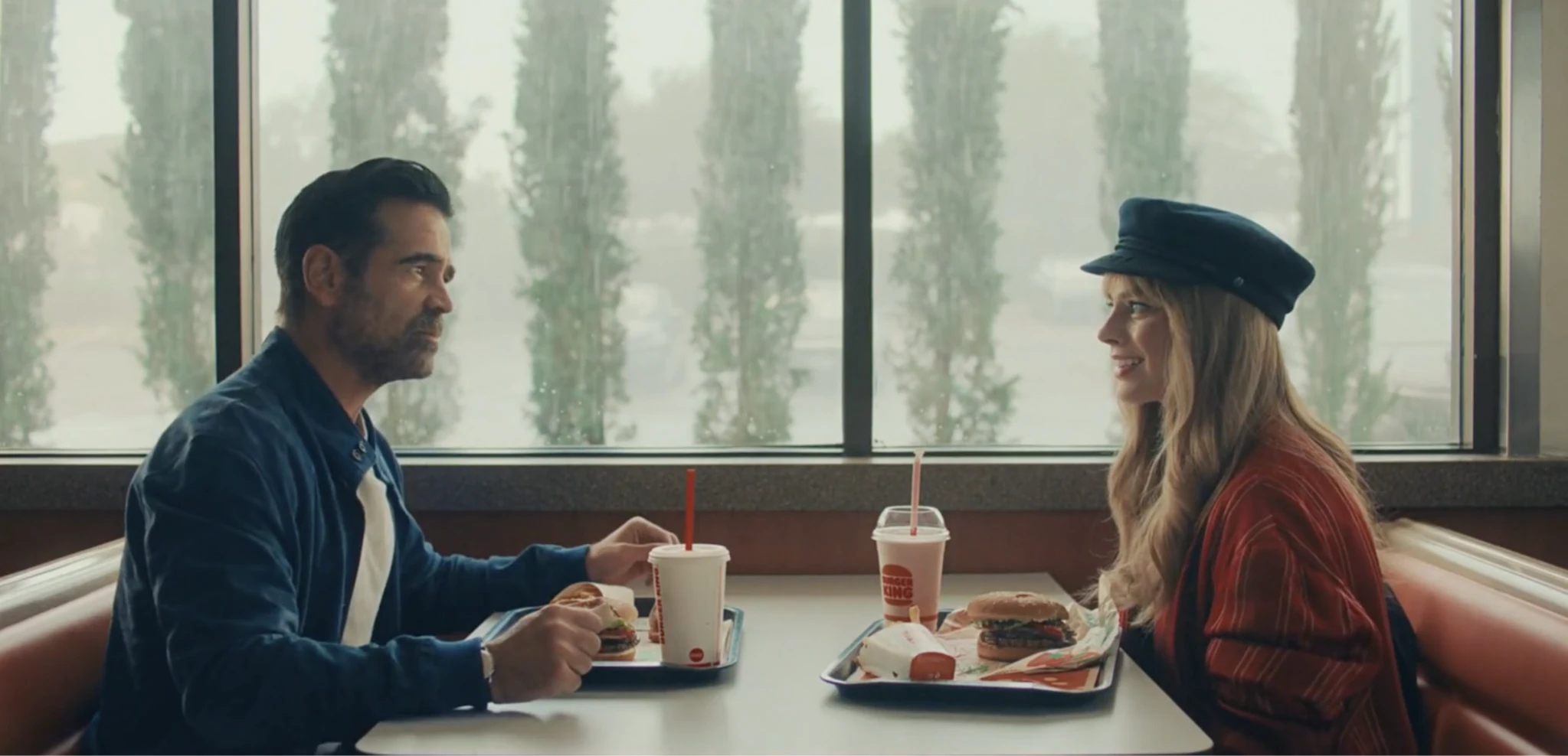 Two characters sit across from each other in a fast-food booth, sharing burgers in a still from A Big Bold Beautiful Journey (2025), directed by Kogonada.