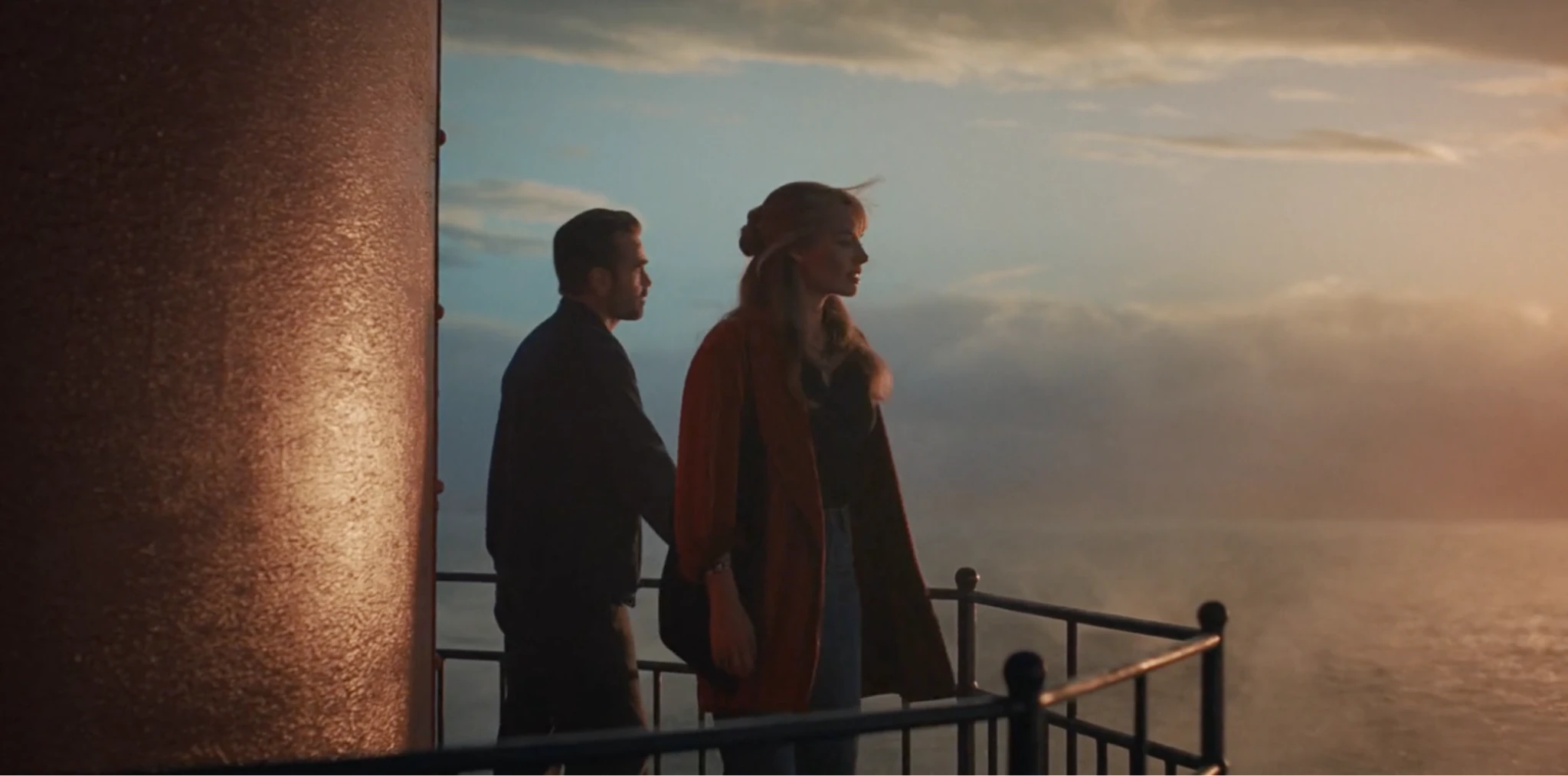 Two characters stand on a lighthouse balcony overlooking the ocean at sunset in a still from A Big Bold Beautiful Journey (2025), directed by Kogonada.