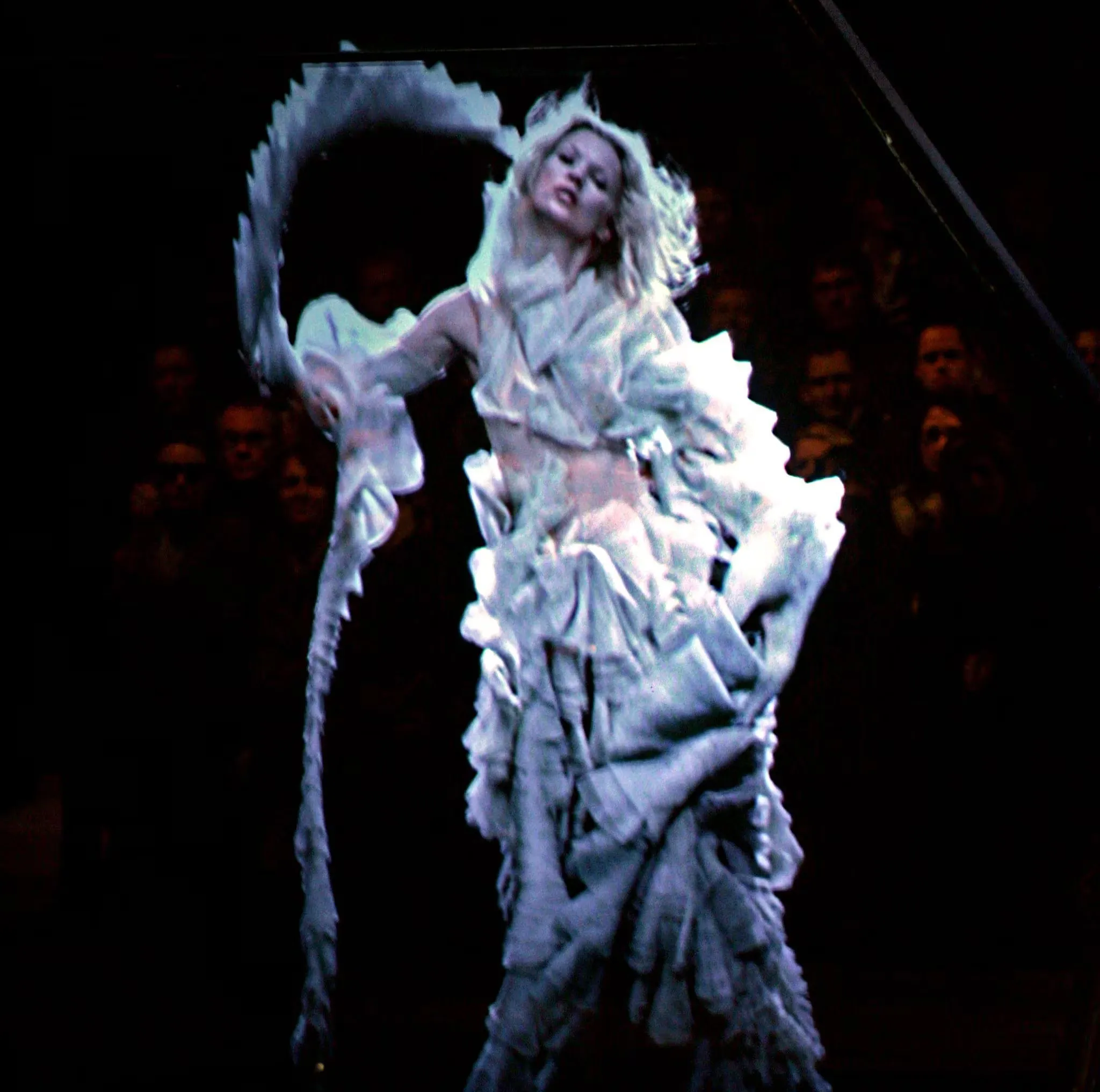 Kate Moss appearing as a hologram during the Alexander McQueen runway show in 2006, suspended within a glass pyramid and surrounded by dramatic theatrical lighting in an iconic fashion moment