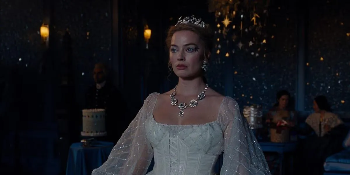 Catherine Earnshaw, portrayed by Margot Robbie, stands in an elegant ballroom wearing a white period gown, tiara and jeweled necklace, surrounded by soft candlelight during a formal evening gathering scene from Wuthering Heights
