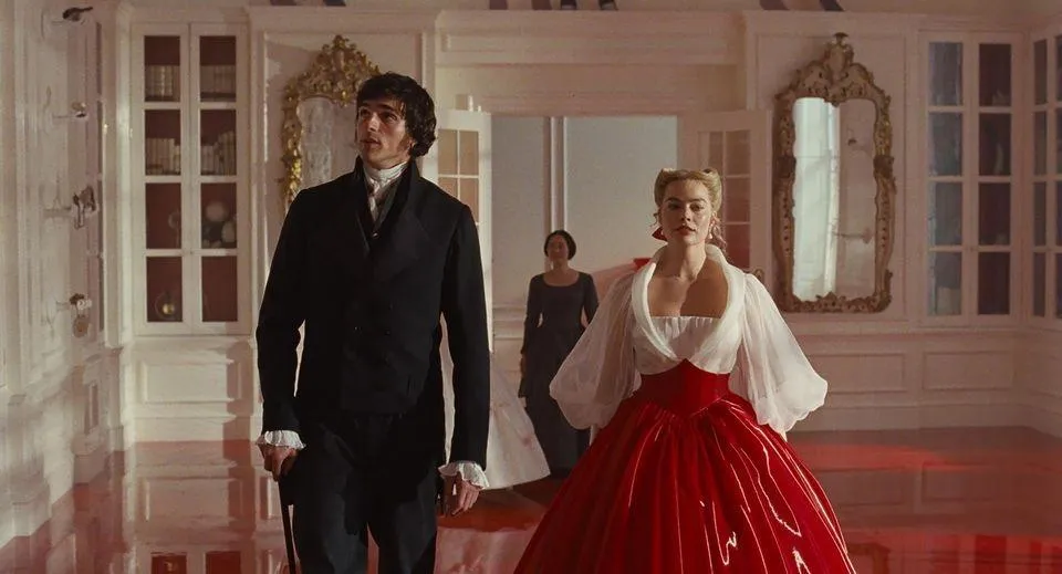 Heathcliff, portrayed by Jacob Elordi, walks beside Catherine Earnshaw, portrayed by Margot Robbie, as Nelly follows behind in a grand interior hallway, evoking a homecoming scene recalling earlier days in Wuthering Heights