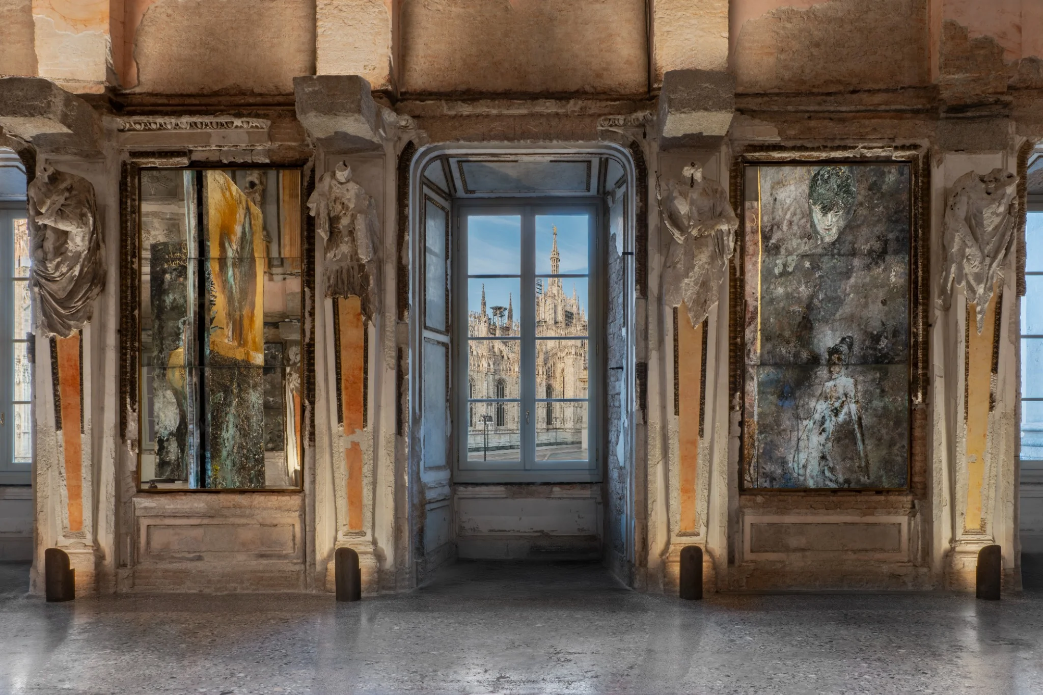 Installation view of Anselm Kiefer’s “The Women Alchemists” at Palazzo Reale, Sala delle Cariatidi, Milan, featuring large-scale textured panels with alchemical and figurative imagery.