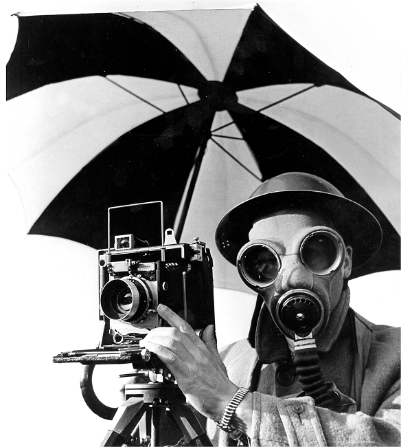 Photographer wearing gas mask and goggles operating large format camera under umbrella