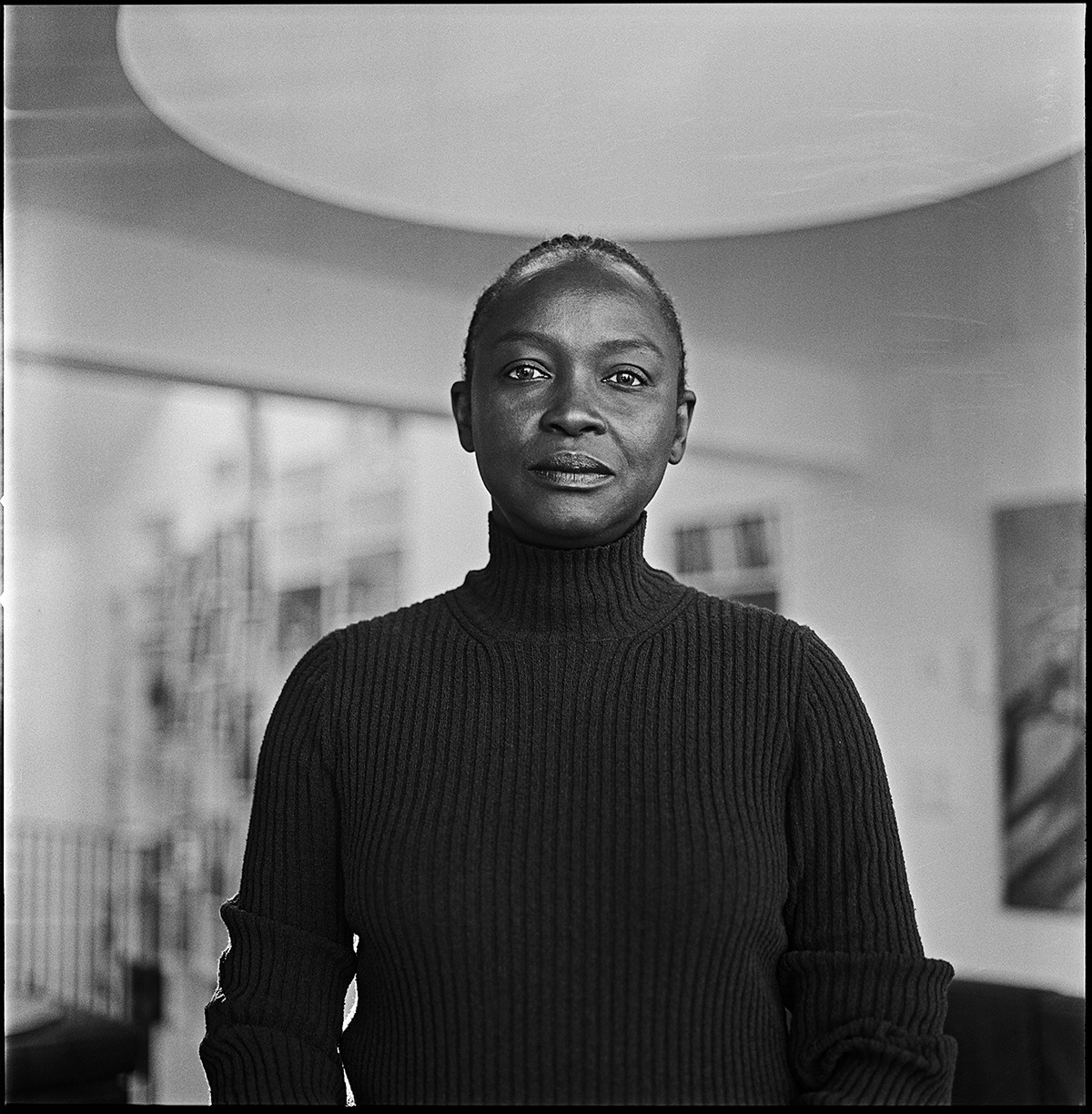 Koyo Kouoh wearing black turtleneck sweater, portrait photograph by Mehdi Benkler