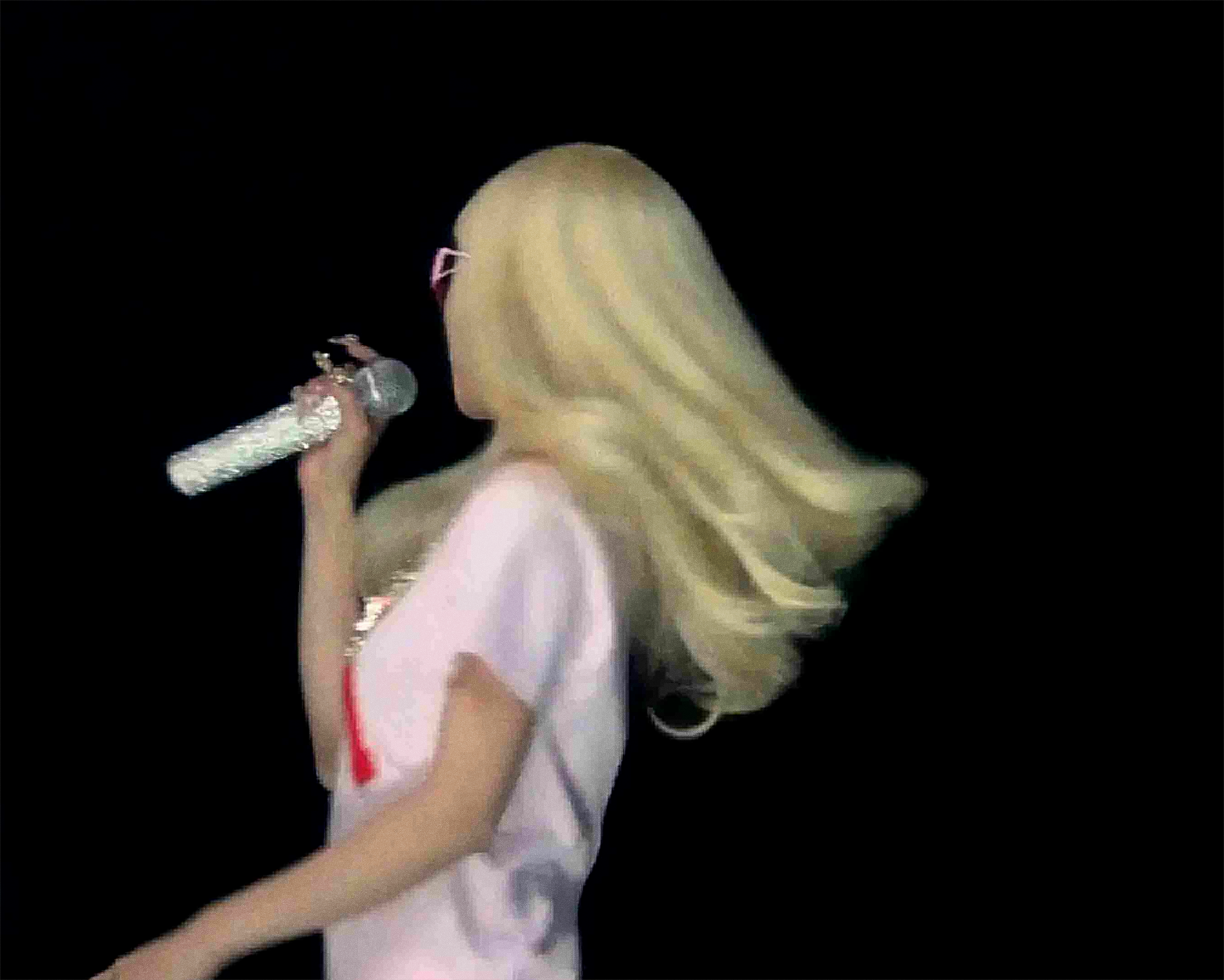 Lexie Liu performing Pop Girl on stage, blonde hair, pink glasses, holding microphone