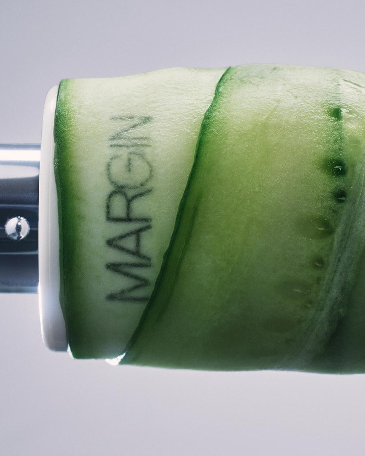 Spiraled cucumber slices wrapped around a glass stamped with Margin brand logo, Michael Kazik photography