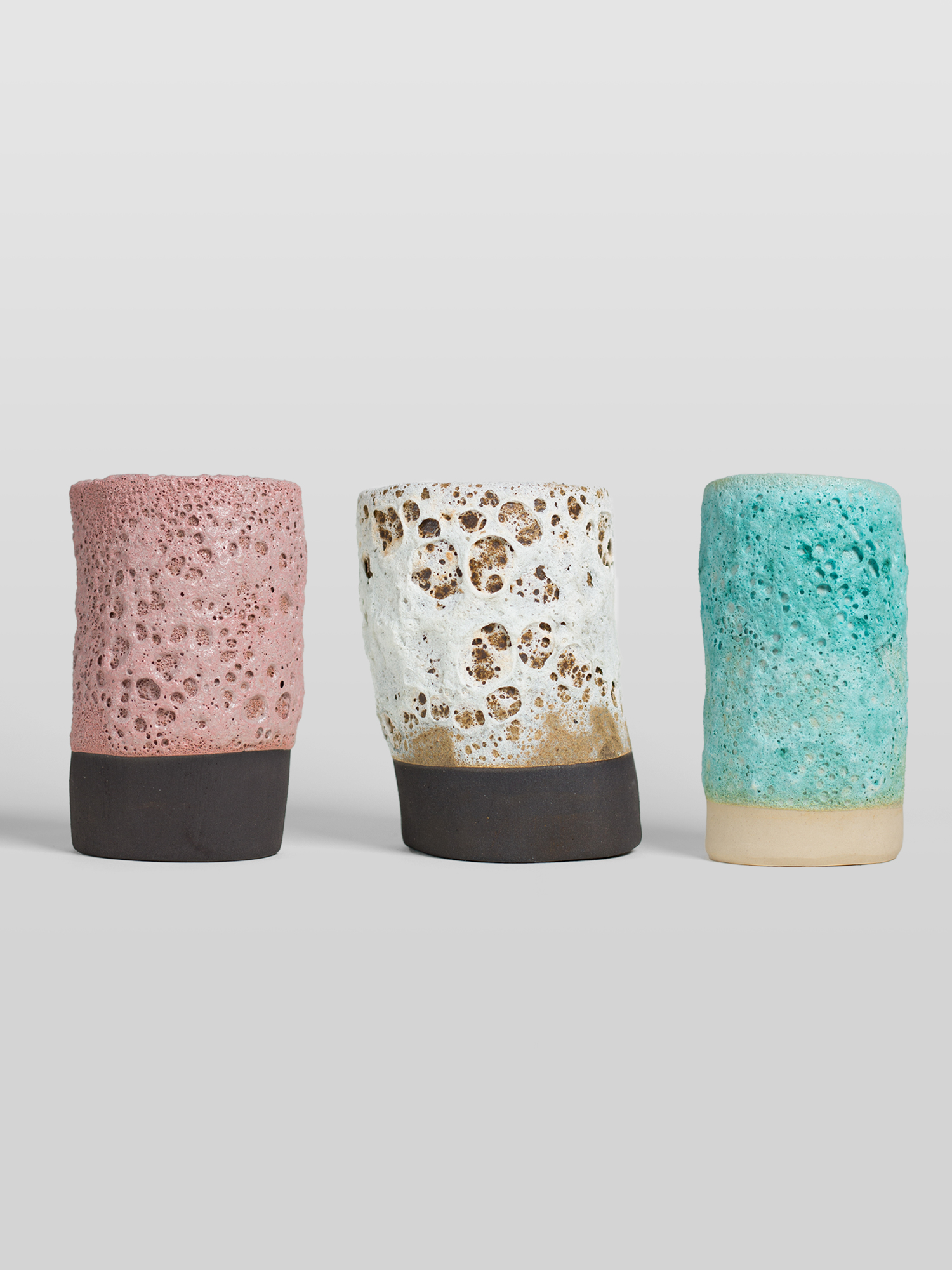 Three GLOST ceramic cups with volcanic lava glaze in pink, white, and turquoise colorways