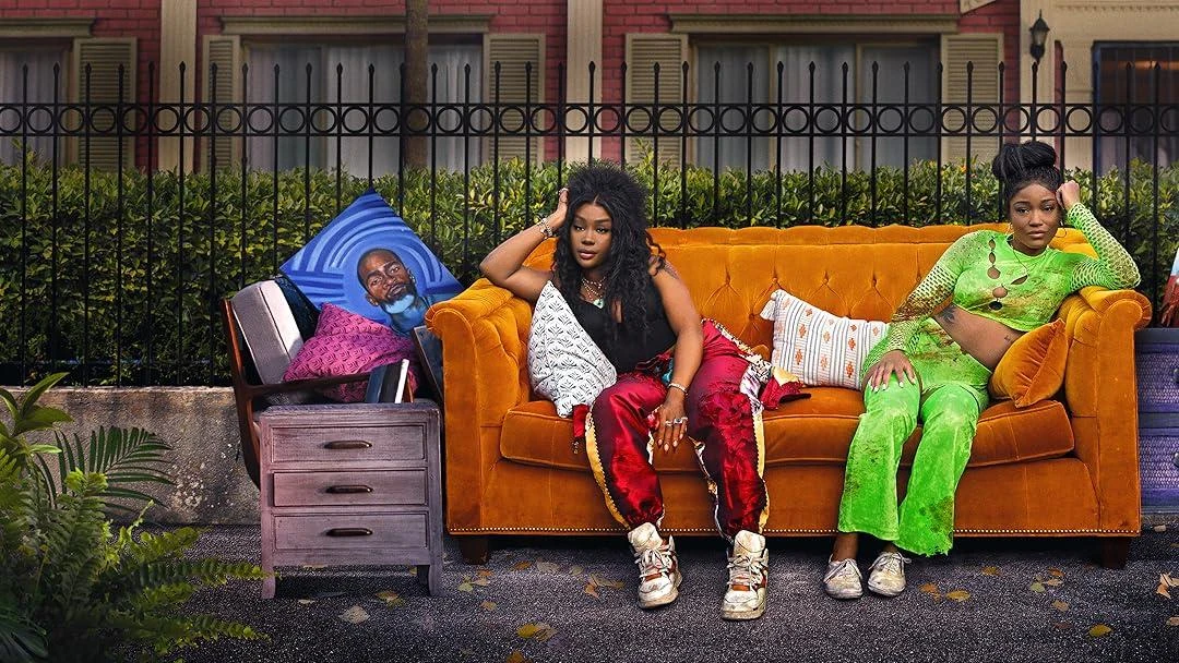 Keke Palmer and SZA pose on an orange couch outdoors in a scene from One of Them Days