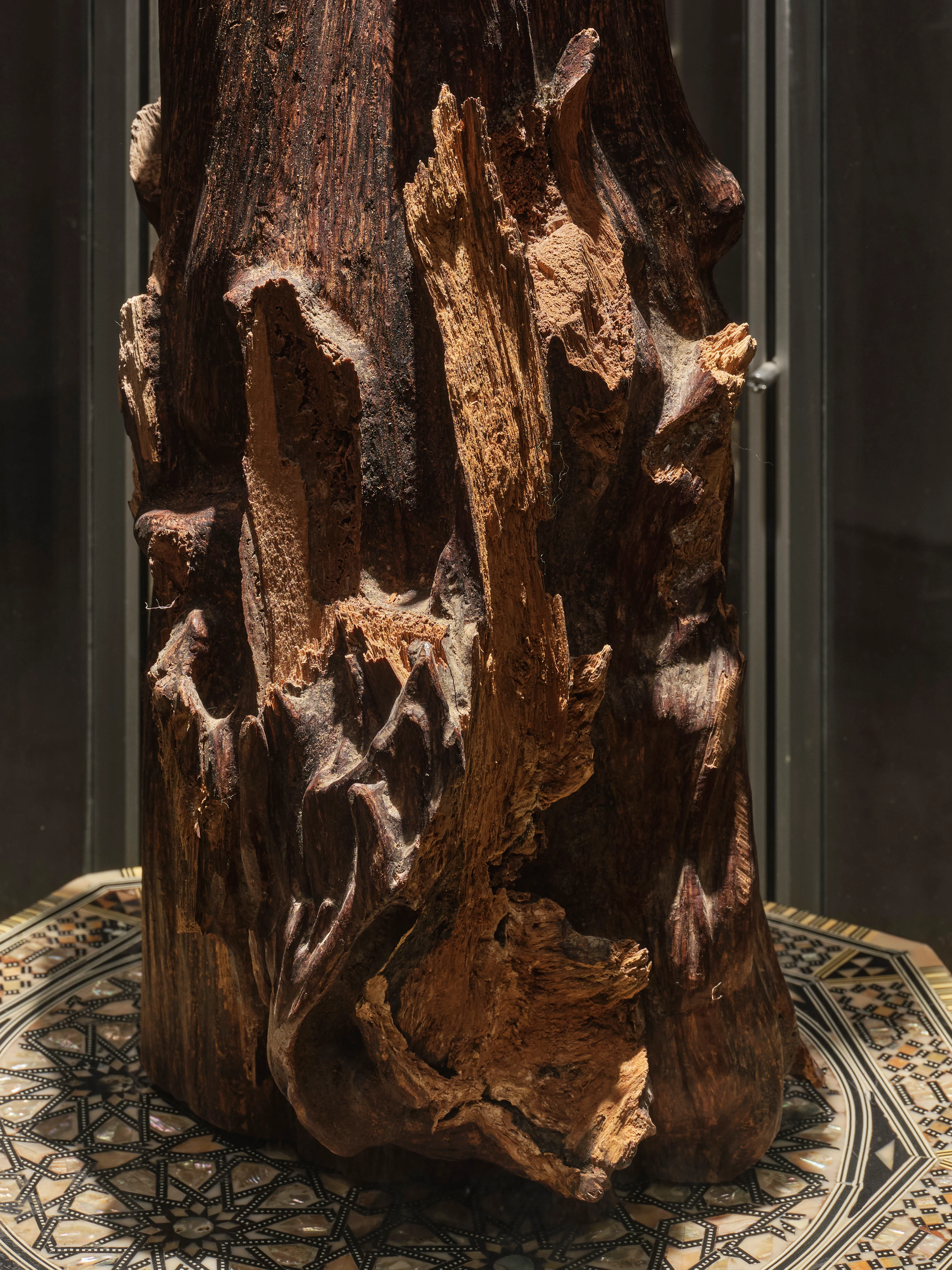 Raw oud wood chunk with natural crevices and resinous grain, displayed on ornate inlaid base for Oud Abaya collection