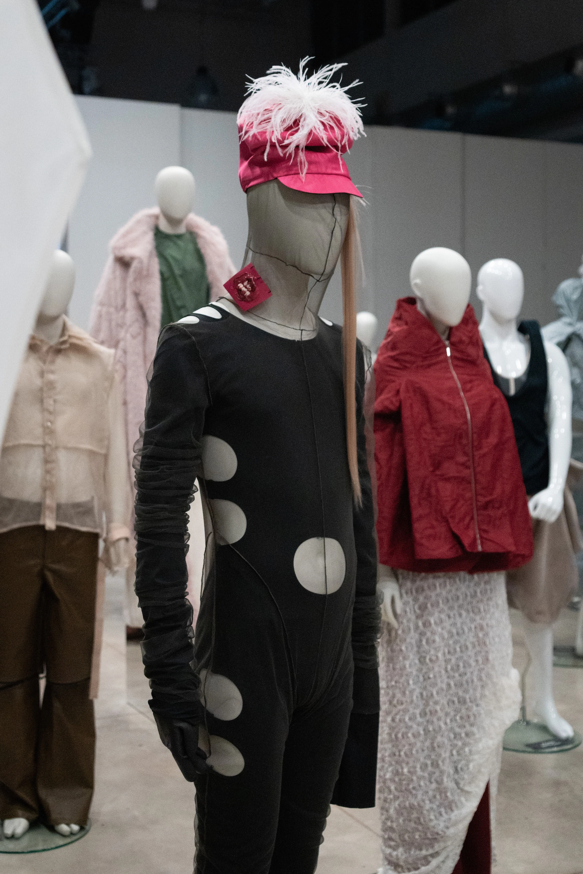 Avant-garde black polka-dot bodysuit with feathered pink cap on mannequin, IED Milan UNFOLD 2026 exhibition by Paolucci & Spacone