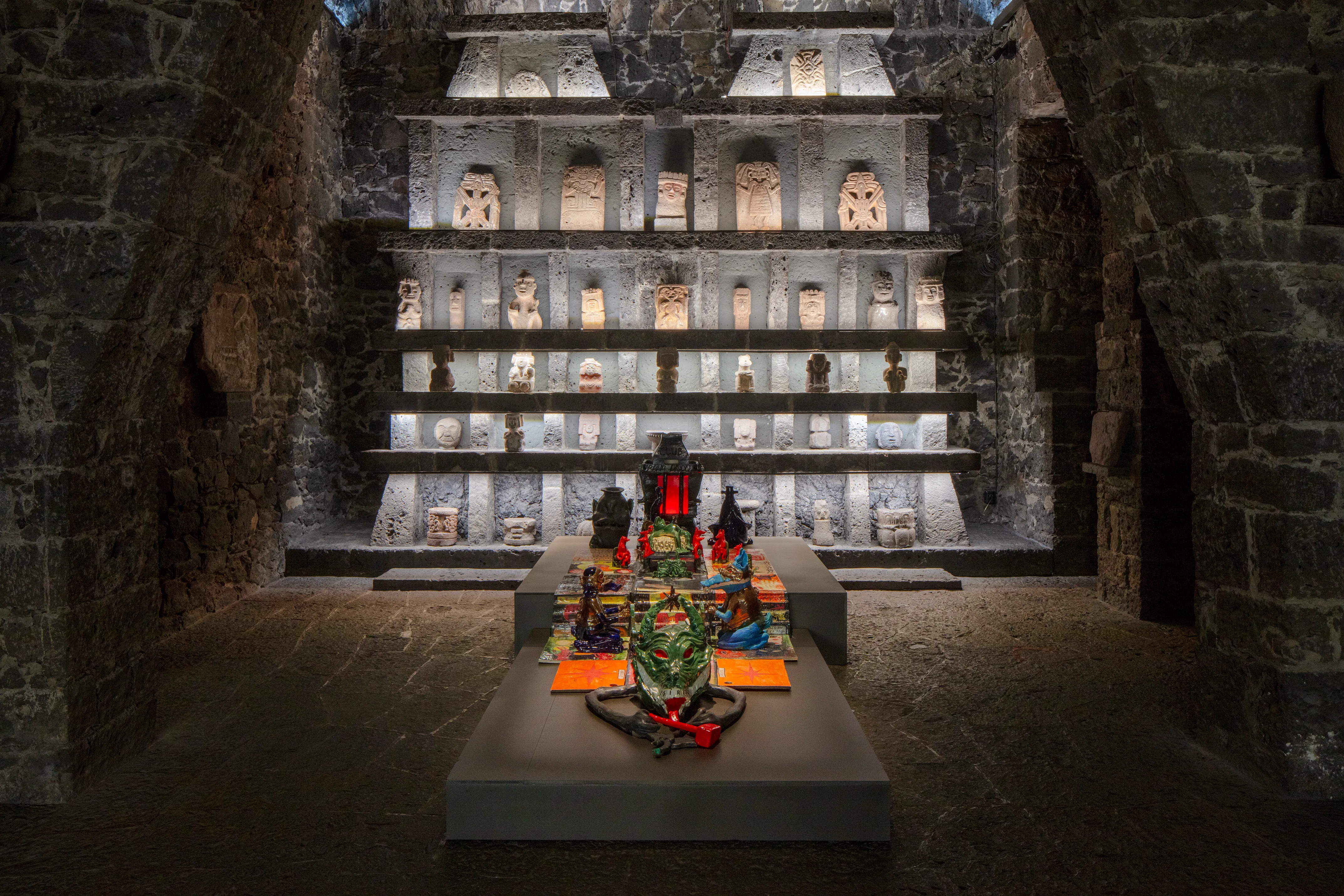 Paloma Contreras Lomas altar installation with pre-Columbian stone figurines in illuminated niches within ancient stone chamber