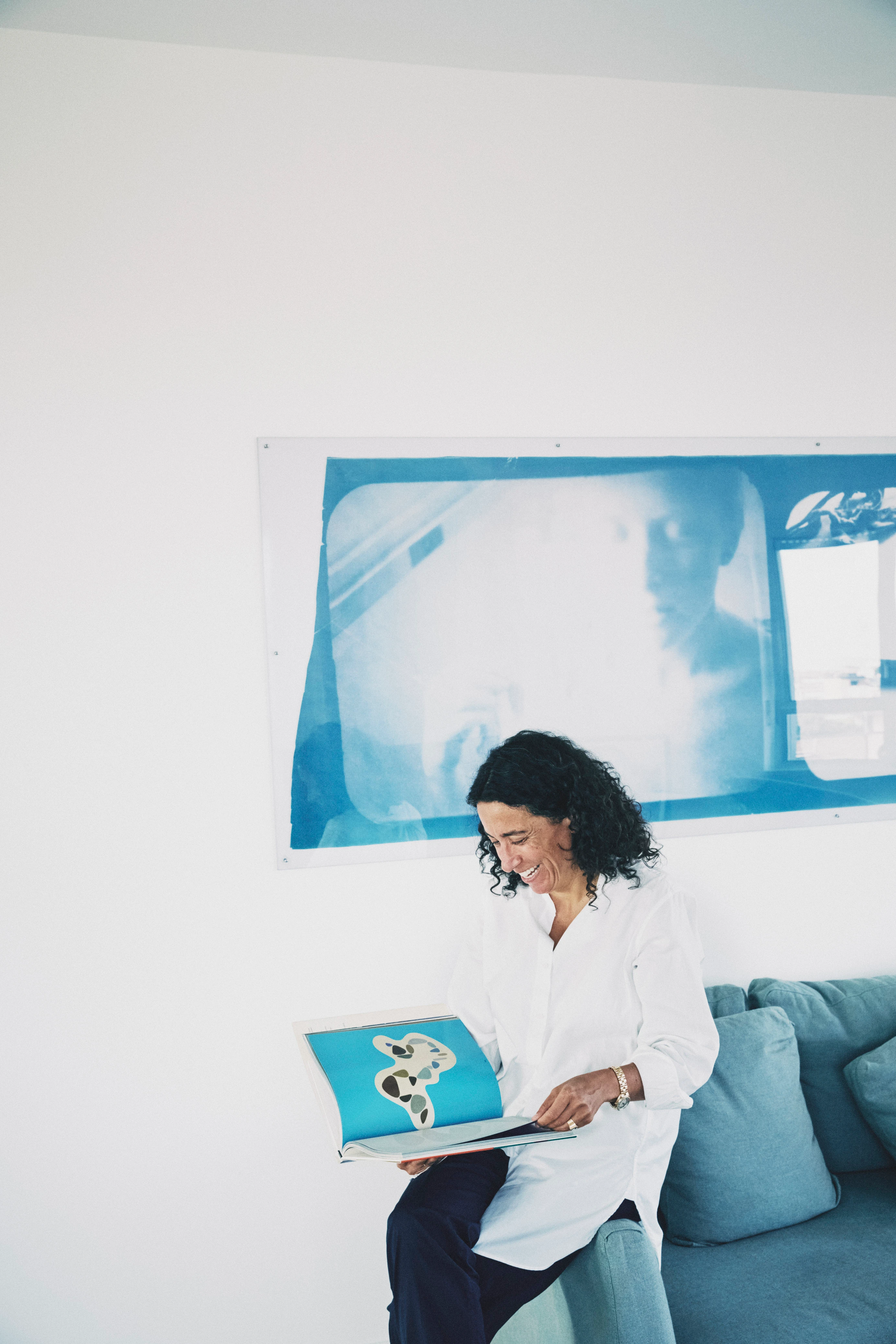 Sara Sozzani Maino smiling while reading an art book at home, photographed by Stefan Gifthaler in 2021