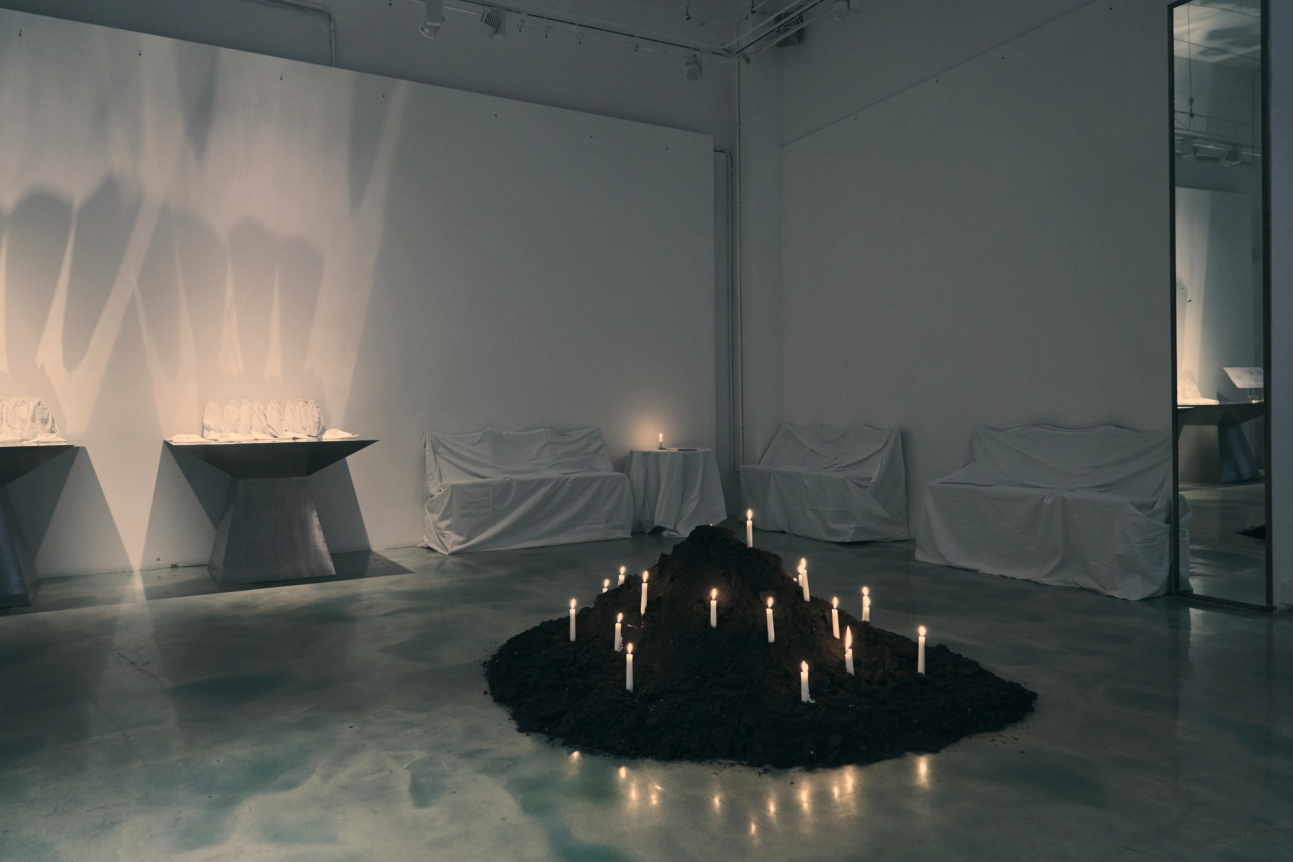 Candlelit soil installation at Fondazione Sozzani Via Piave 33 collection presentation, white-draped furniture in gallery