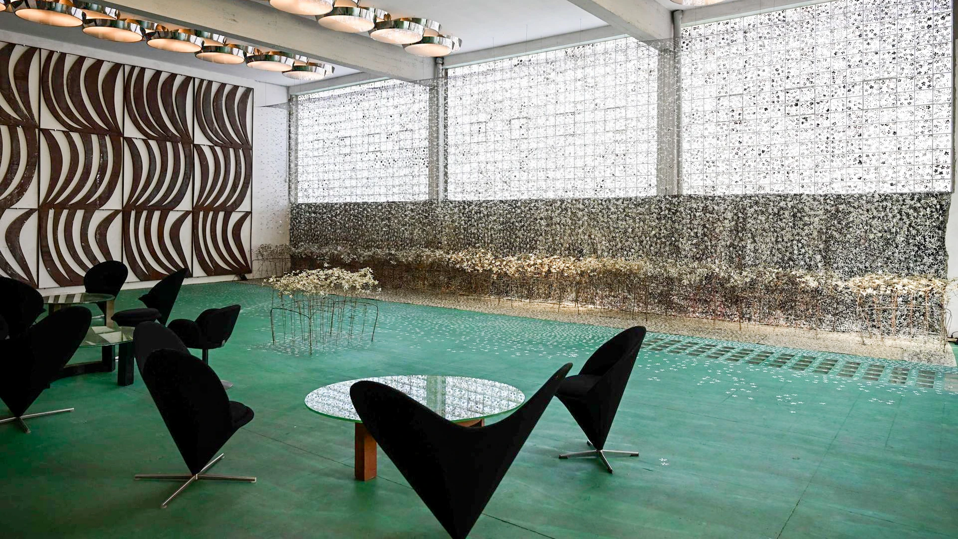 Fondazione Sozzani Milan event space with cone chairs, green floor, mosaic walls, and wavy wood panels