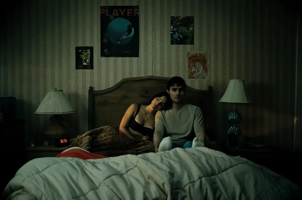 Nikki leans on Bear in a dim moody bedroom, a tender yet unsettling scene from Focus Features.