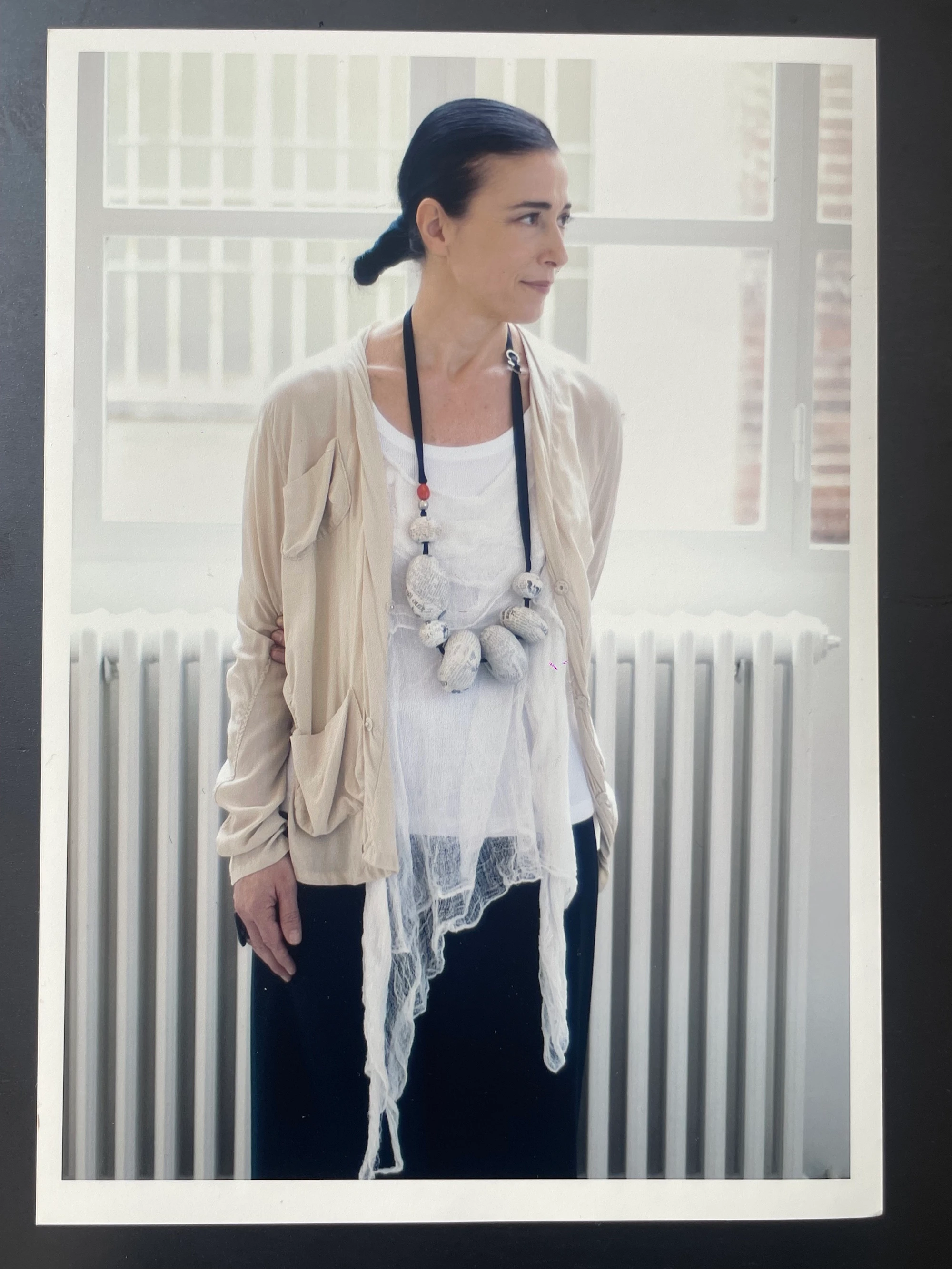 Maria Calderara standing by window in beige jacket and sculptural stone necklace, portrait by Sebastiano Pavia