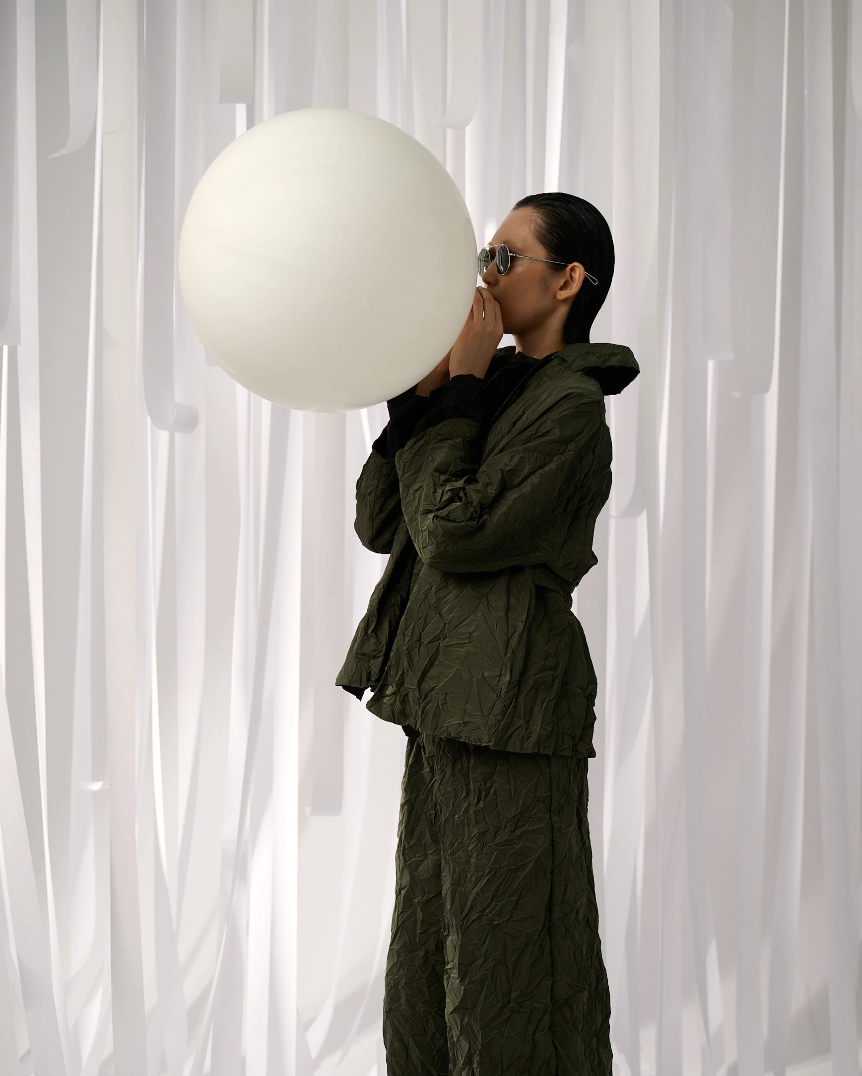 Maria Calderara SS25 Touch collection model in olive crinkled suit blowing oversized white balloon