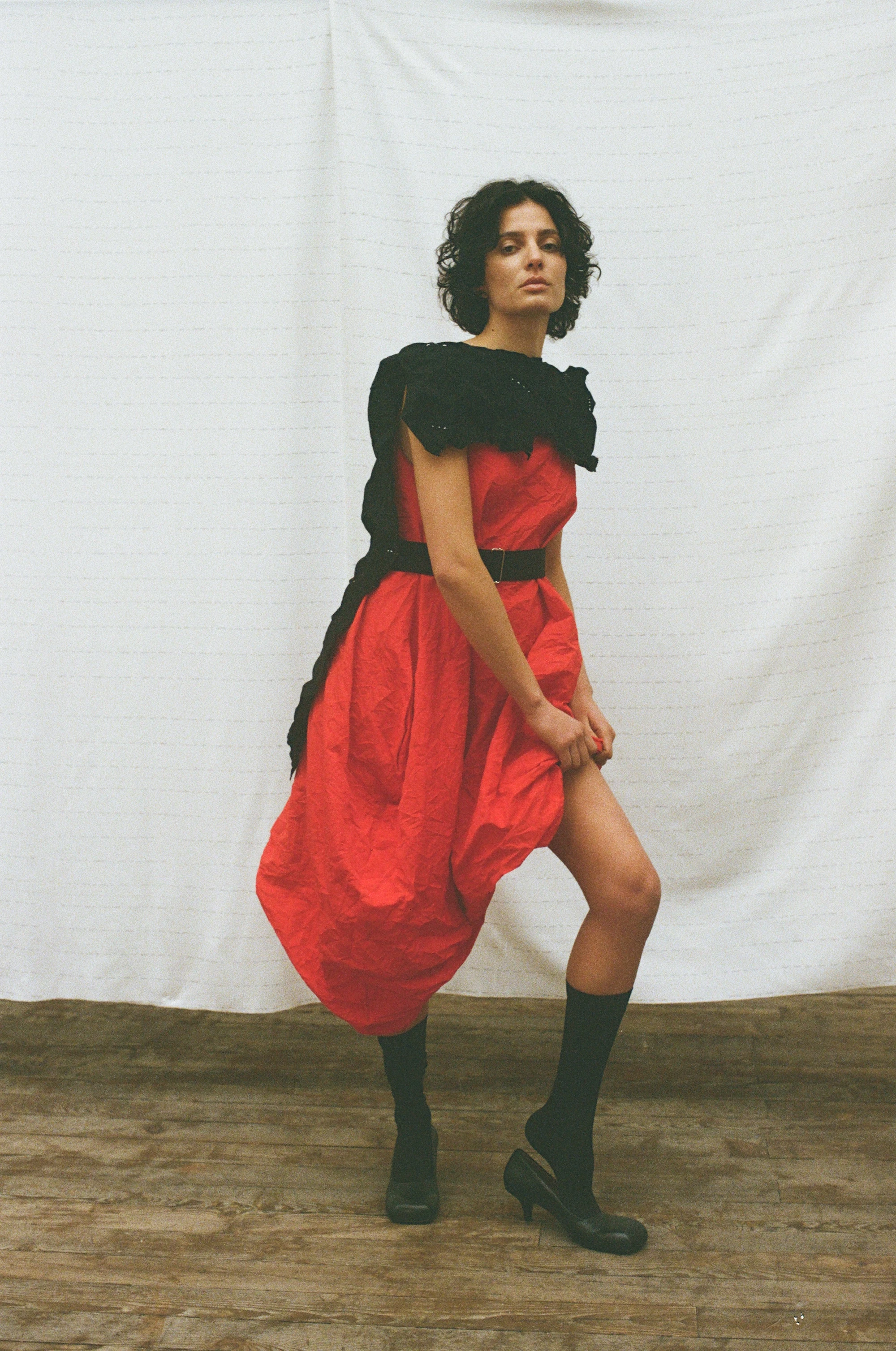 Maria Calderara F/W 26 look: bold red balloon dress with black ruffle collar, belt, and knee-high heeled boots