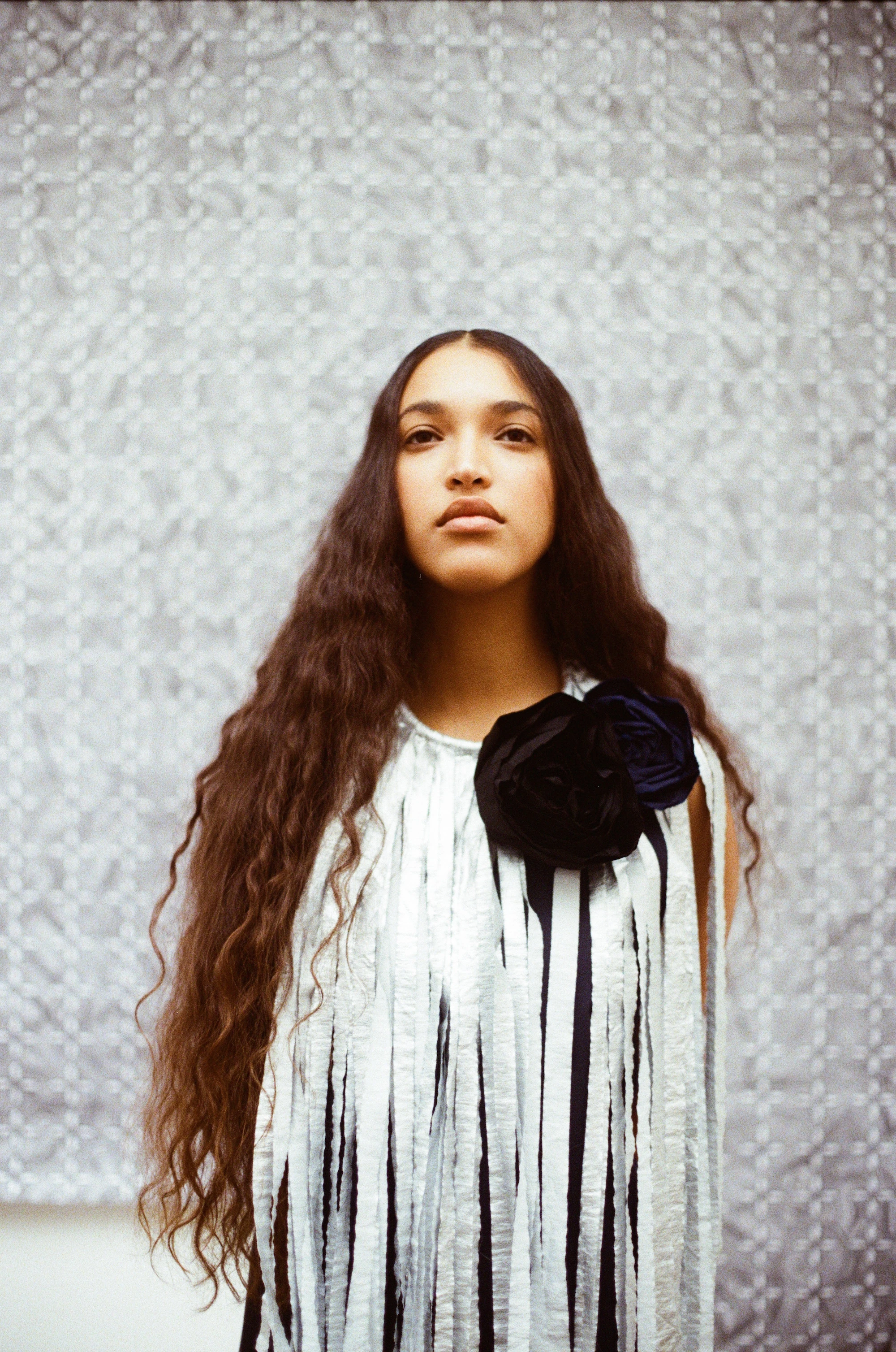 Model in Maria Calderara F/W 26 striped top with velvet rosette, long wavy hair, lace backdrop