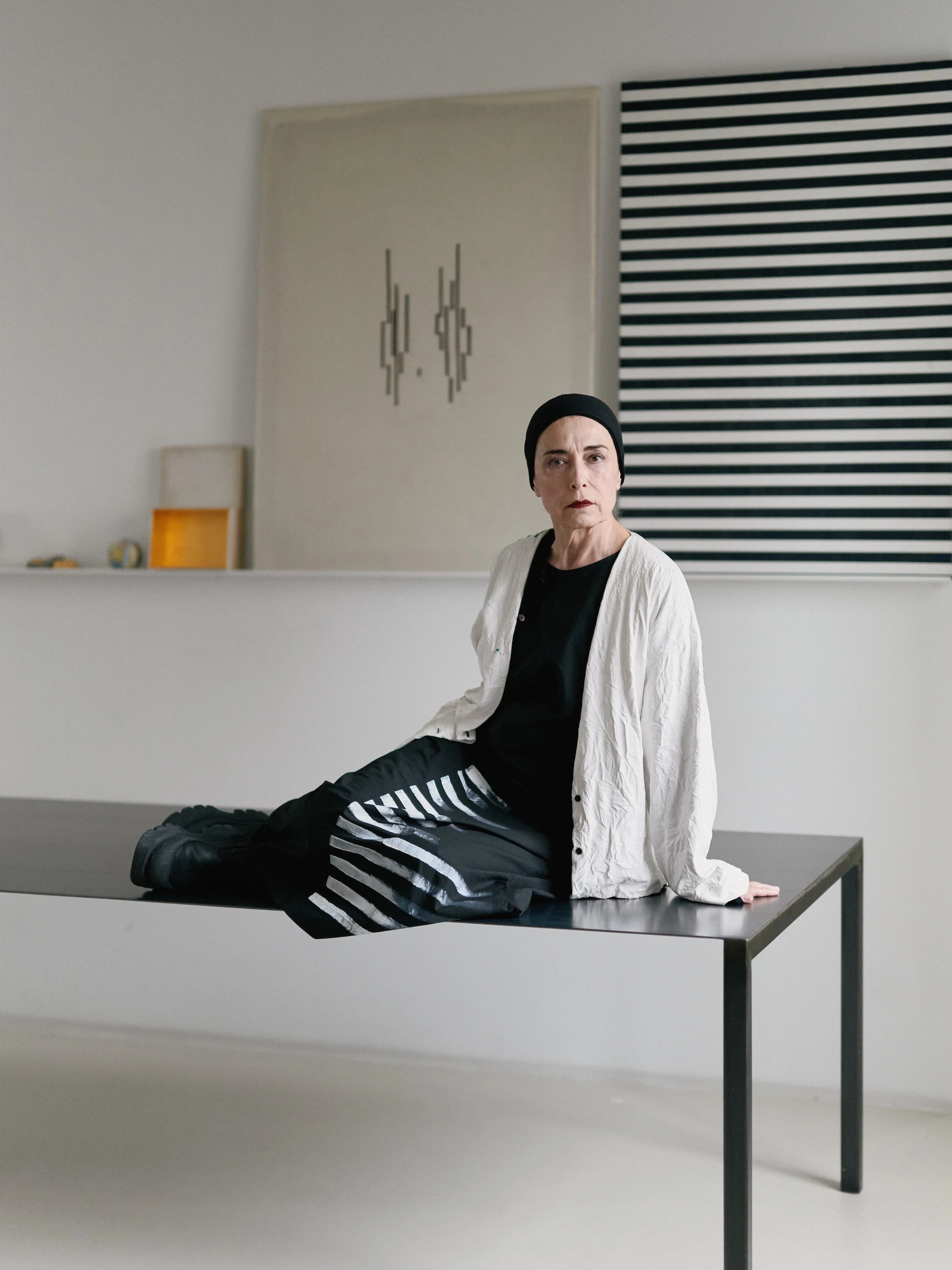 Fashion designer Maria Calderara seated on a table in her minimalist studio, photographed by Lorenzo Morandi.
