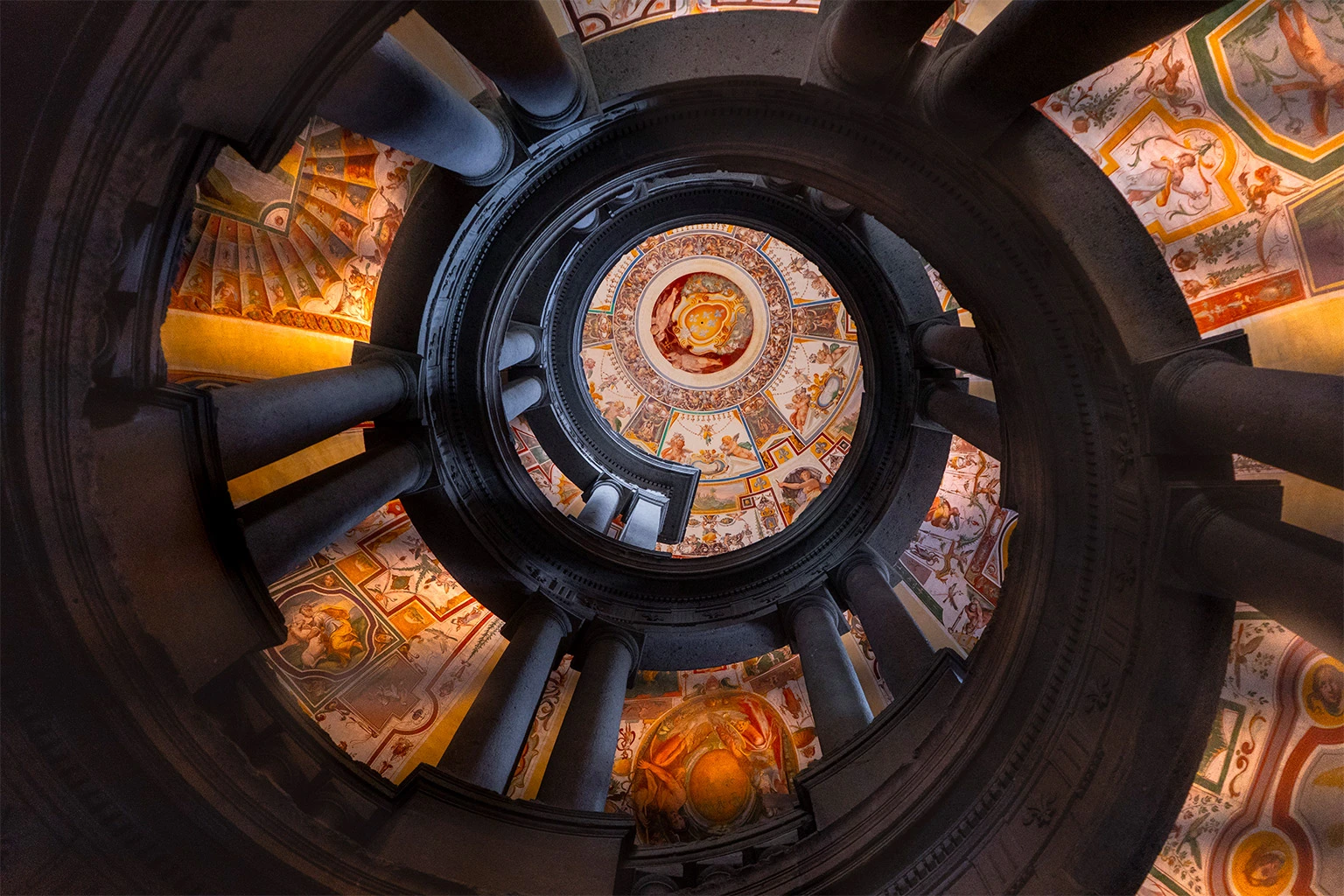 Looking up through the spiral staircase of the Scala Regia, Palazzo Farnese Caprarola, with ornate Renaissance frescoes on the walls