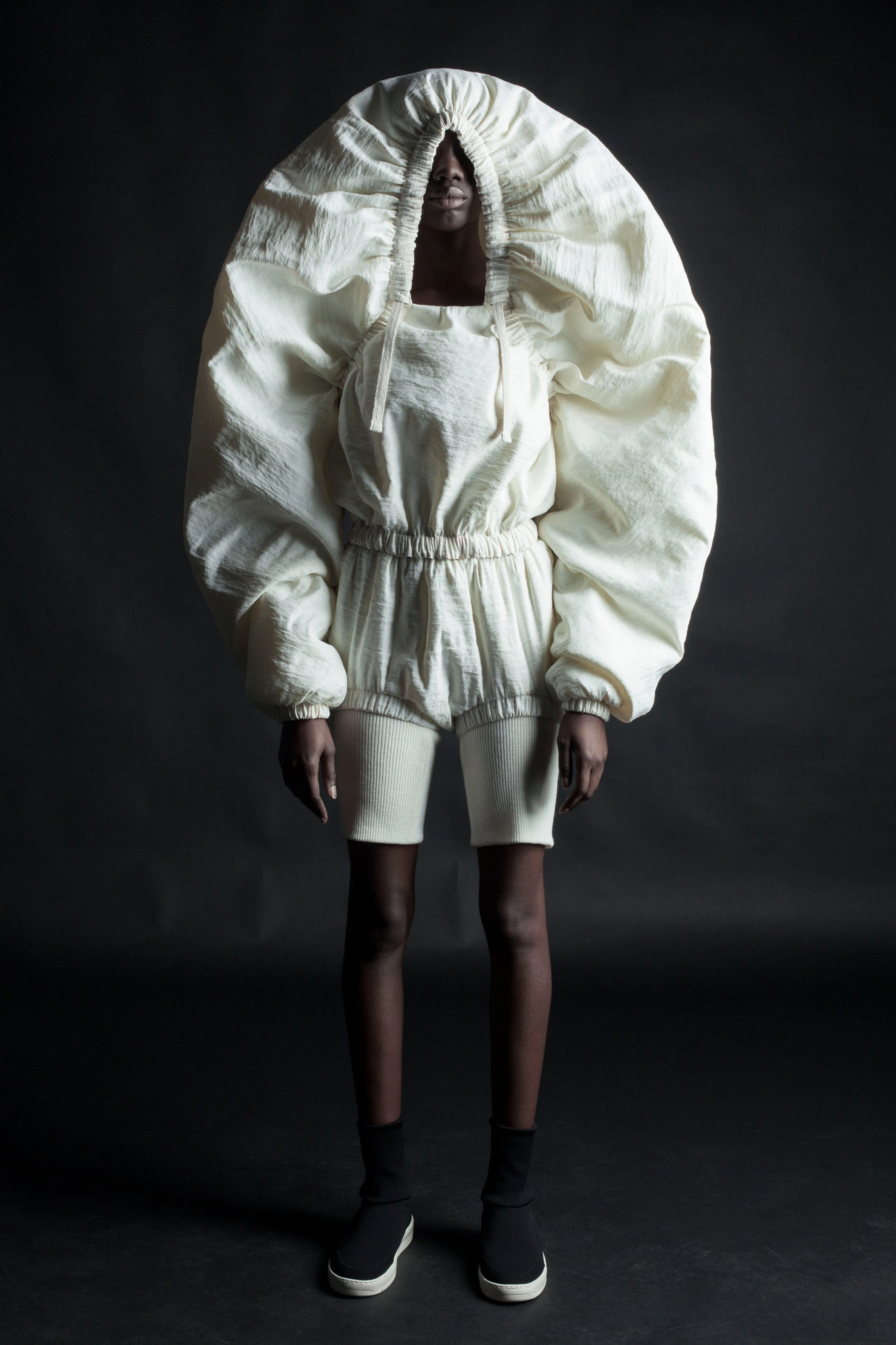 DZHUS AW 2020 Misconcept collection: sculptural ivory puffer ensemble with oversized oval hood, shorts, and black sneakers