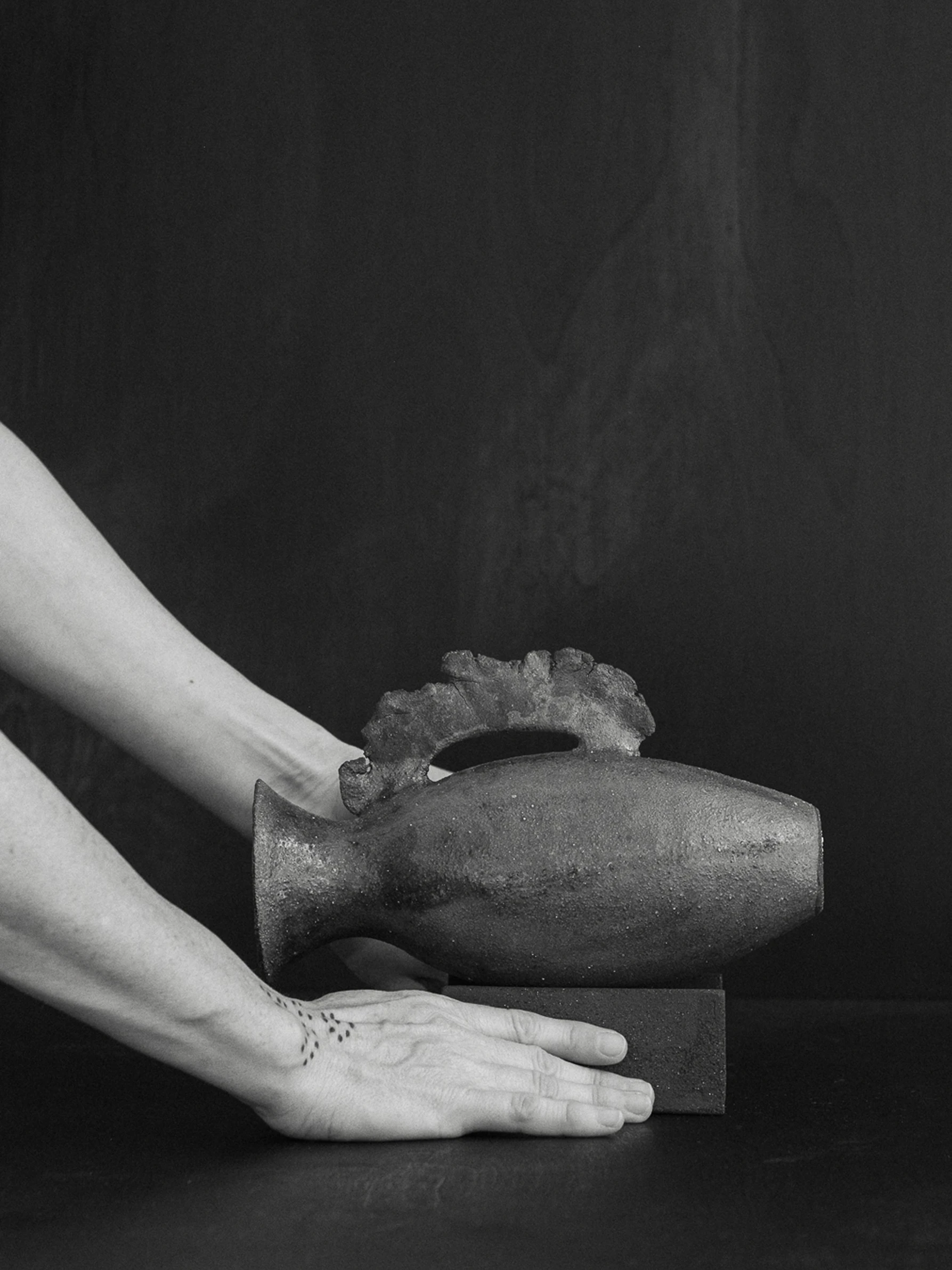Miriam Cernuda arranges a dark textured ceramic vessel on a stone plinth, photographed by Holly Fielder
