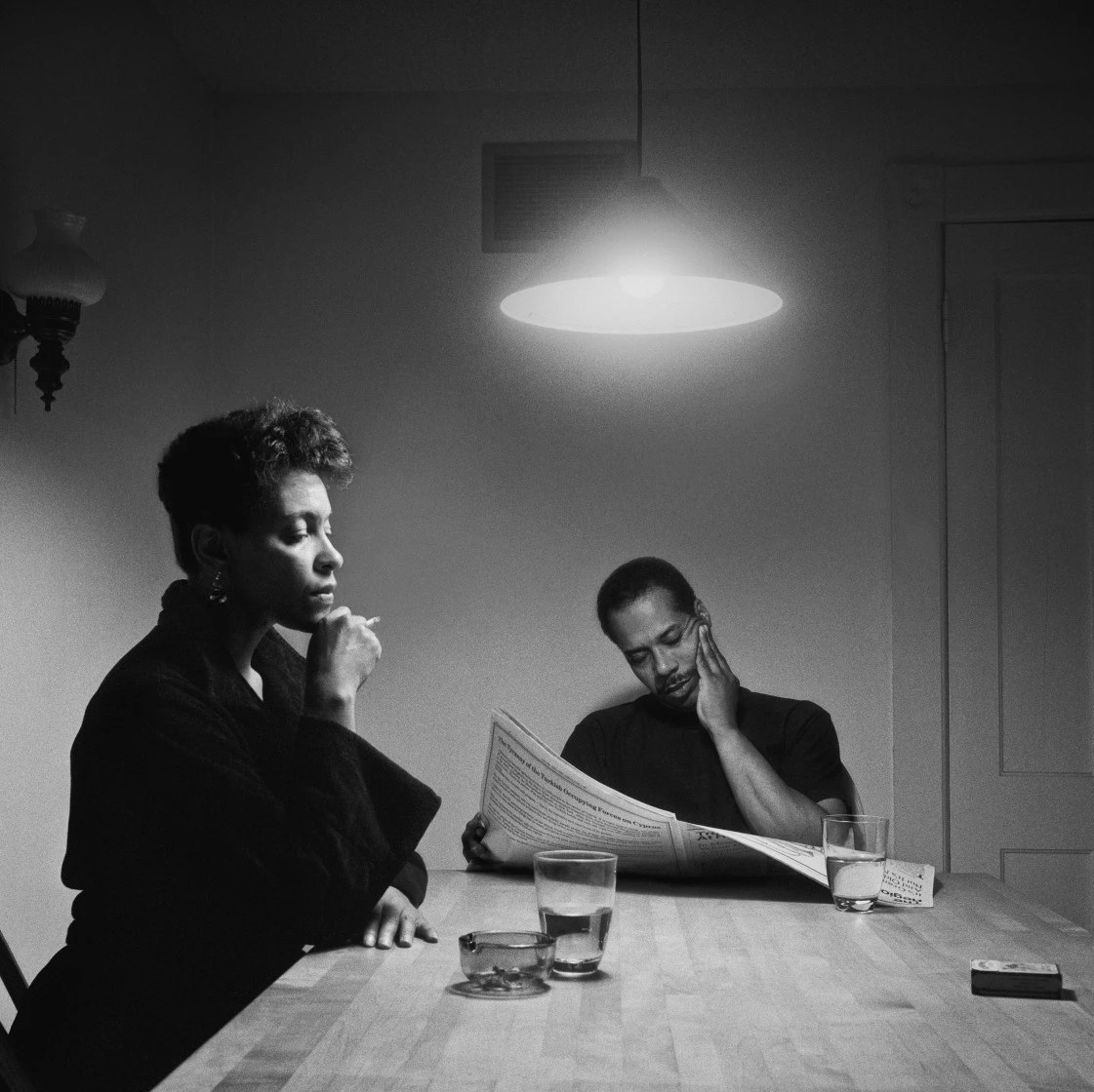 Carrie Mae Weems' The Heart of the Matter: two figures at a table under a pendant lamp in black and white