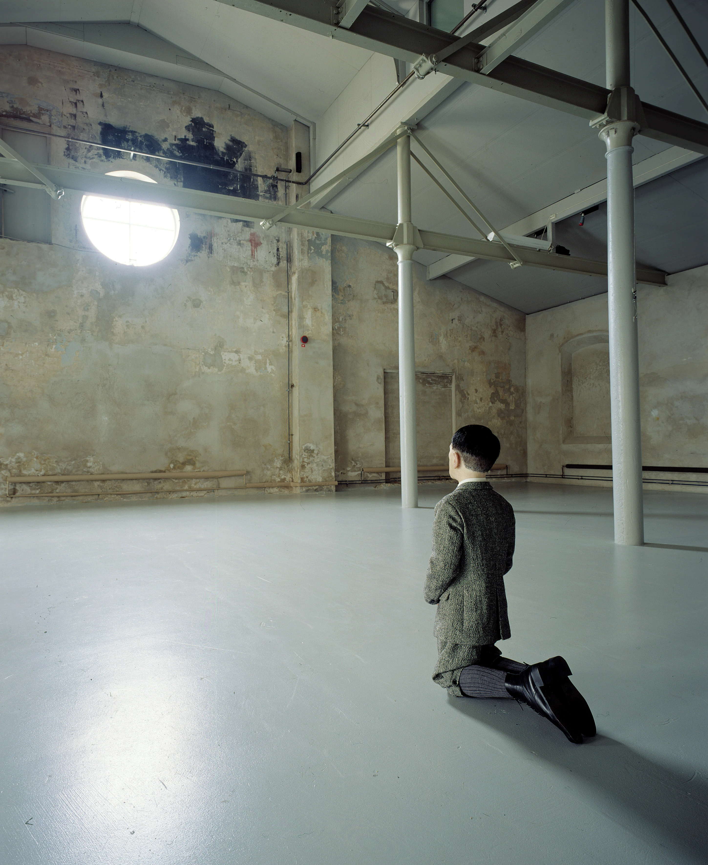 Maurizio Cattelan's Him, 2001 — small figure kneeling alone in vast deteriorating industrial space, photo by Attilio Maranzano