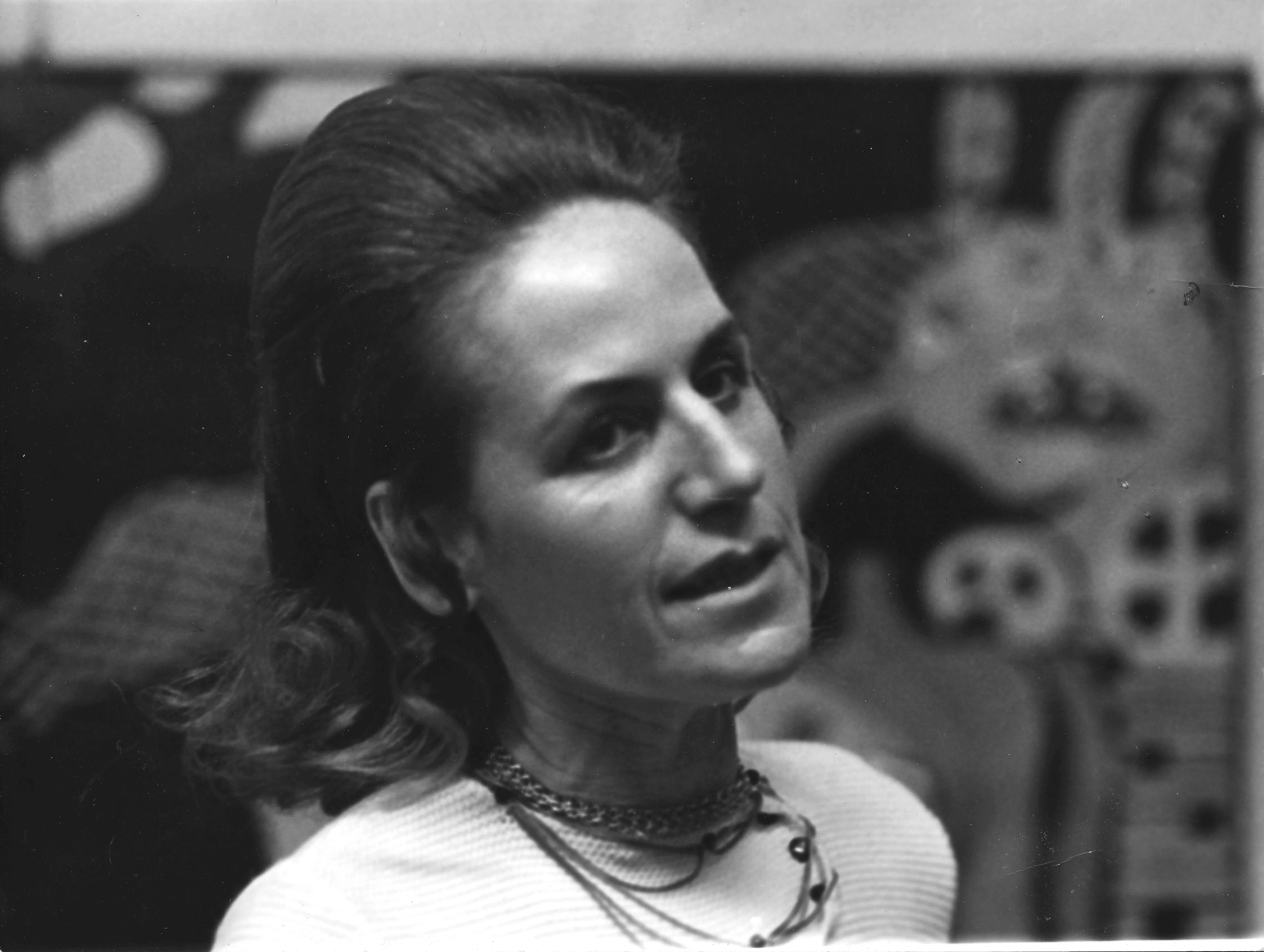 Clemen Parrocchetti, Italian artist, photographed in Milan in 1974, with abstract artwork visible in the background.