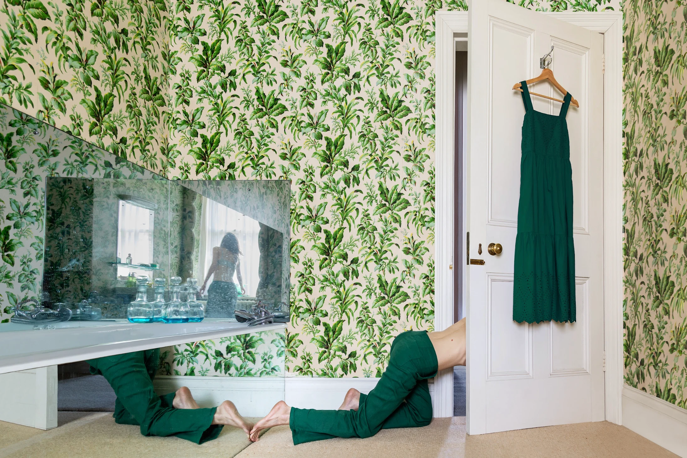 Magorzata Dawidek Holding Patterns 2025 — figure in green beneath mirrored console, botanical wallpaper, dress on door