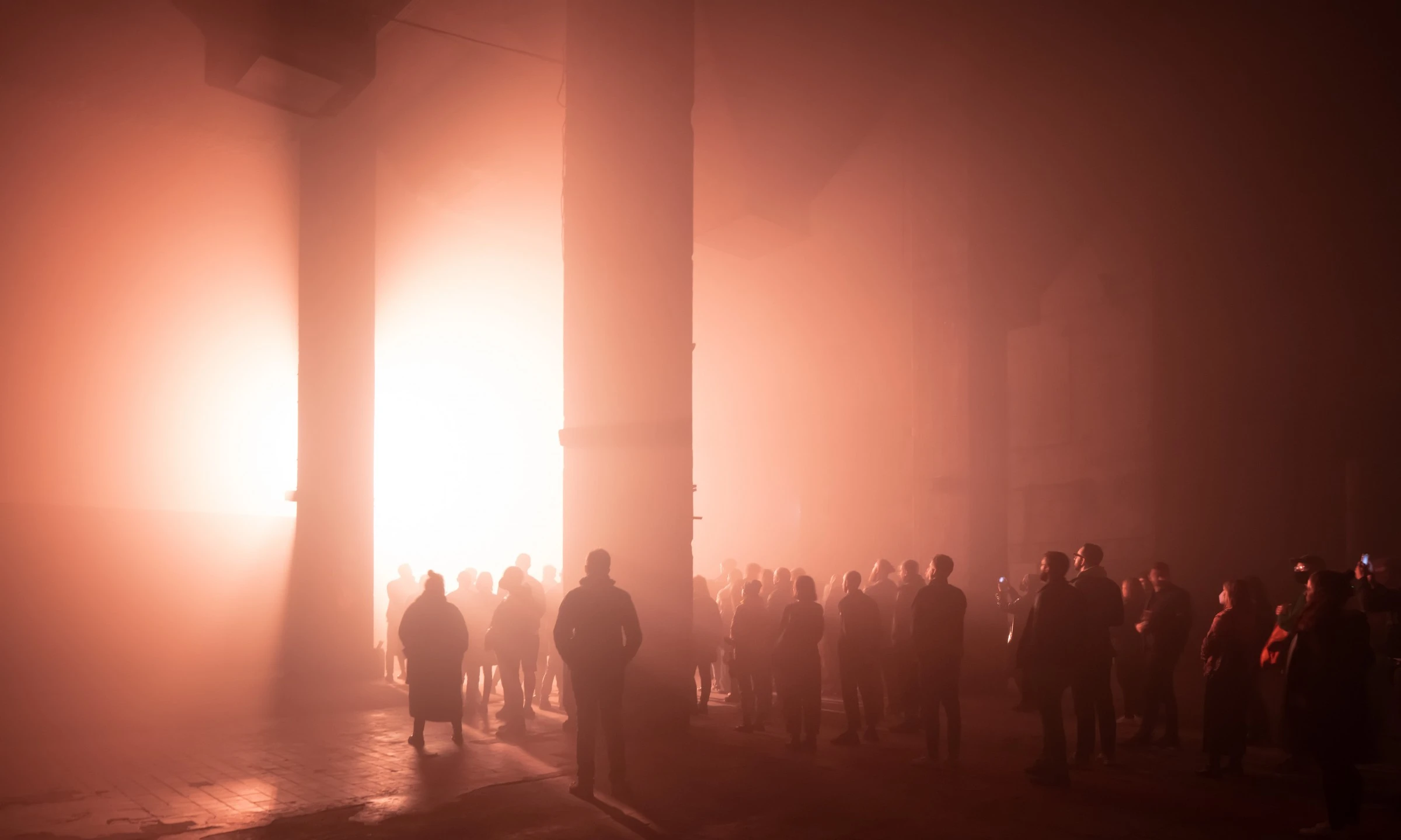 Crowd of silhouettes bathed in warm red fog inside Halle am Berghain, Berlin, for Ian Cheng's Life After Bob, 2022