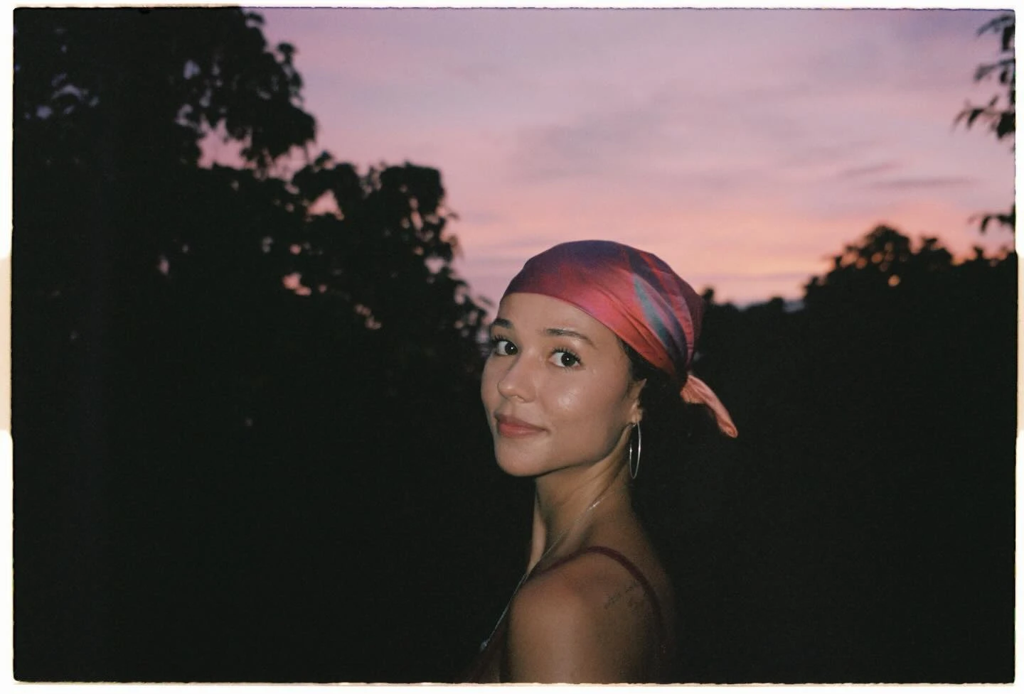 Breanna Yde glancing over her shoulder at sunset, wearing a colorful headscarf and hoop earrings