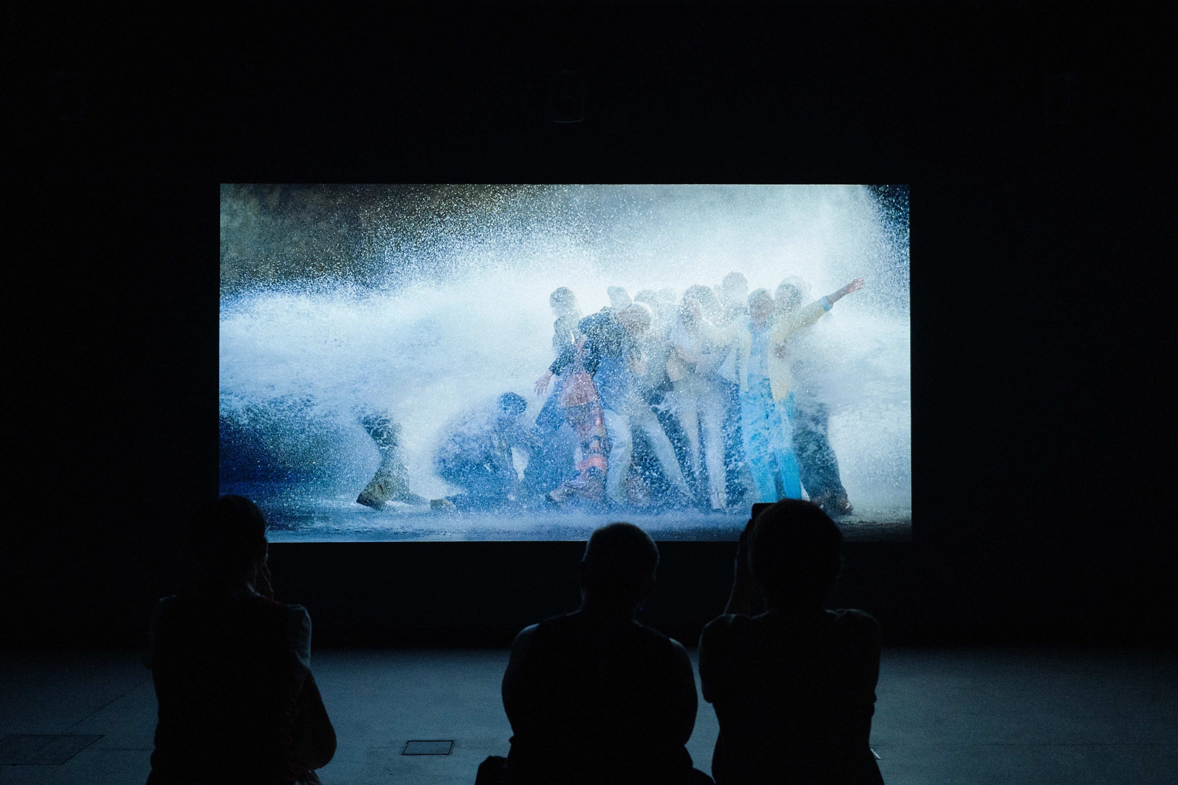 Bill Viola video installation showing figures engulfed by crashing water projected on large screen in darkened gallery