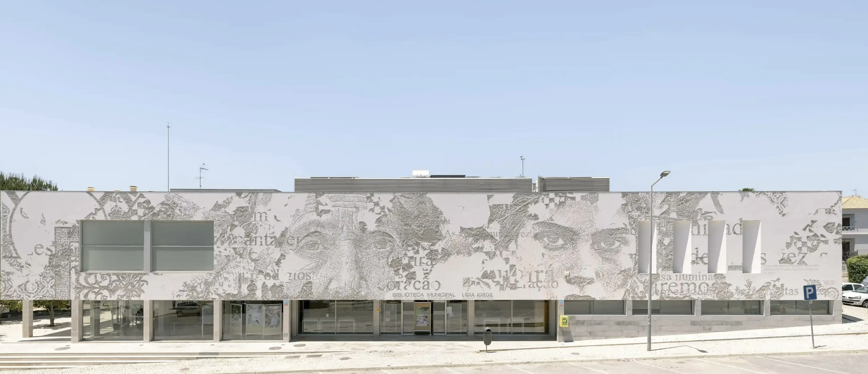 A large library featuring a striking monochromatic mural on its external wall showcases parts of human faces and fragments of large text.