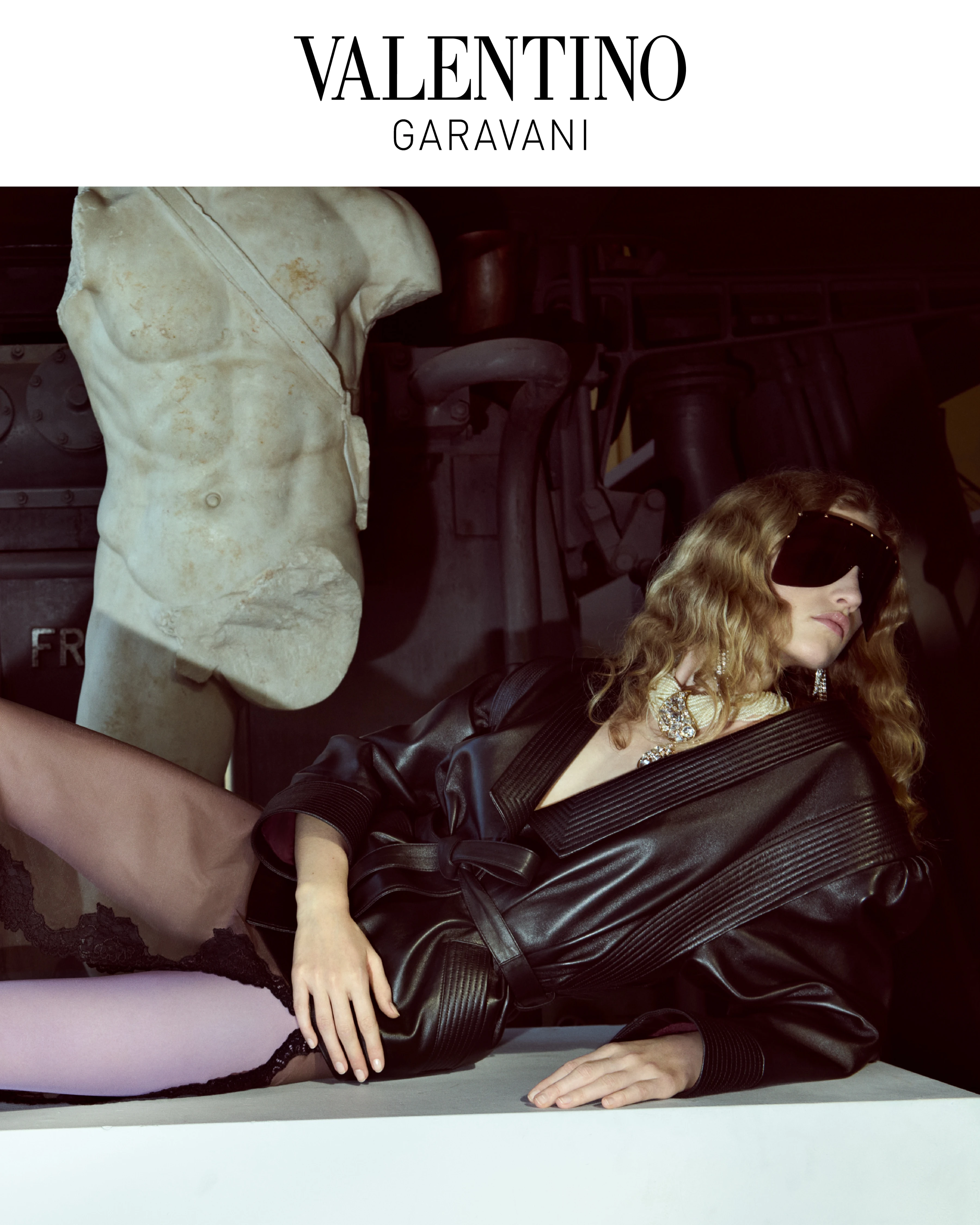 Valentino Garavani FW26 Interferenze campaign: model in black leather jacket, oversized sunglasses, pink tights beside marble torso