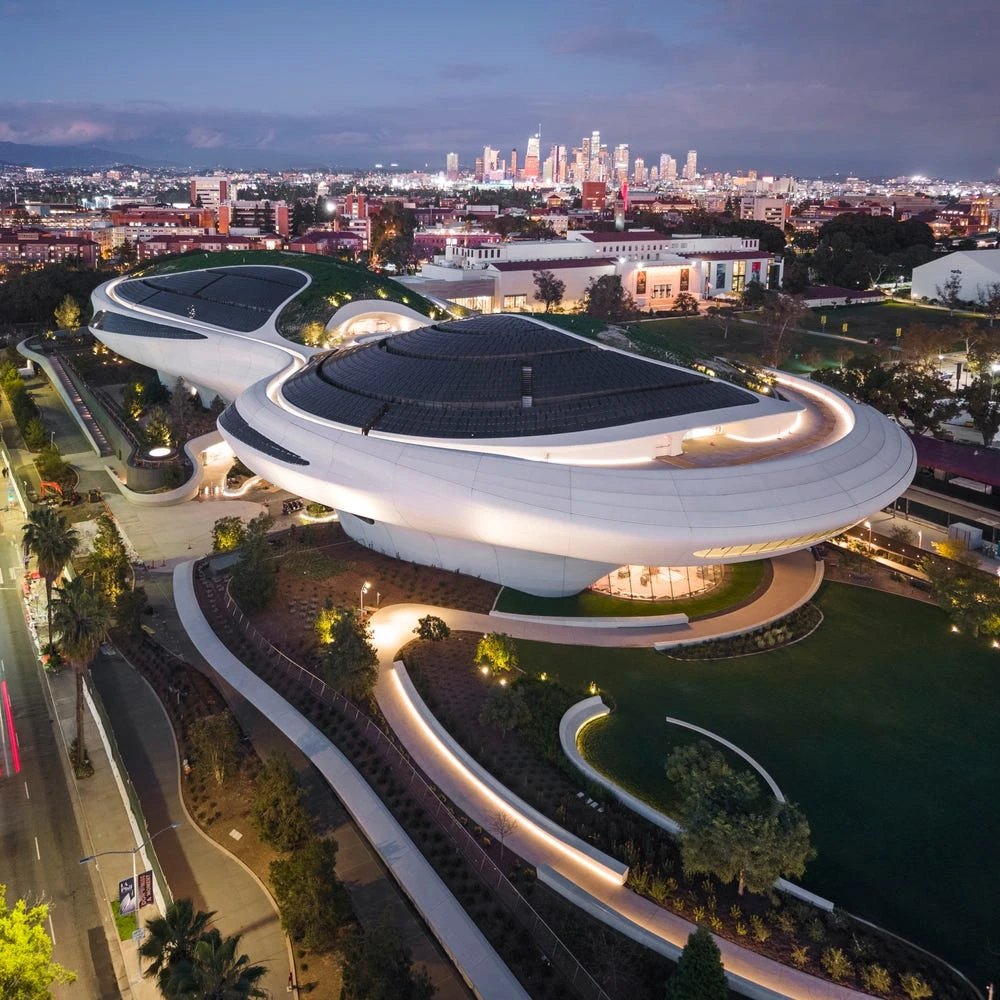 Lucas Museum of Narrative Art glowing white organic architecture aerial view at dusk with Los Angeles skyline