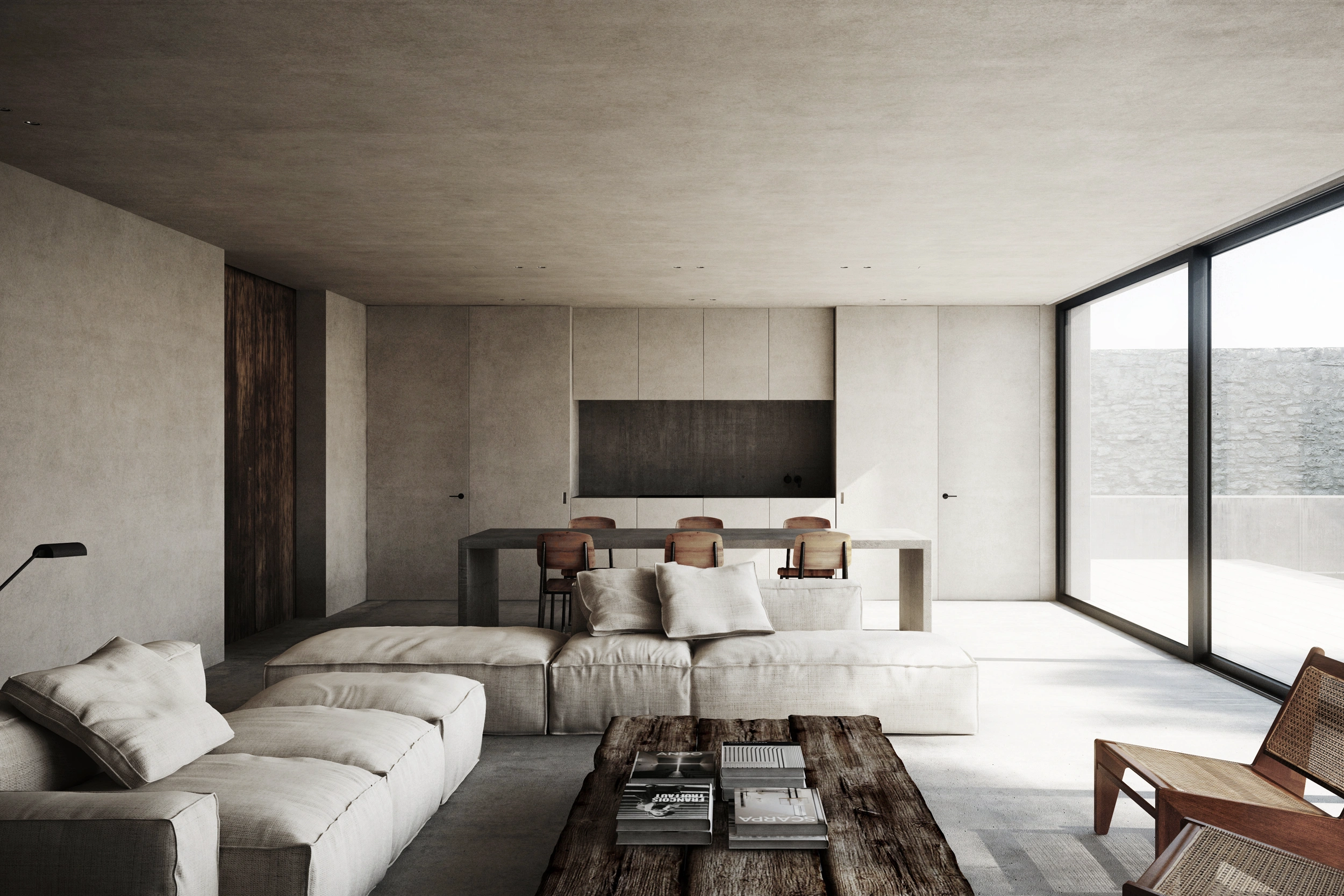 Minimalist living and dining space with concrete walls and ceiling, a linen sectional sofa with throw pillows, a rustic reclaimed-wood coffee table with books, a rattan armchair, a dining table with wooden chairs, and floor-to-ceiling windows overlooking a stone courtyard.Nicolas Schuybroek