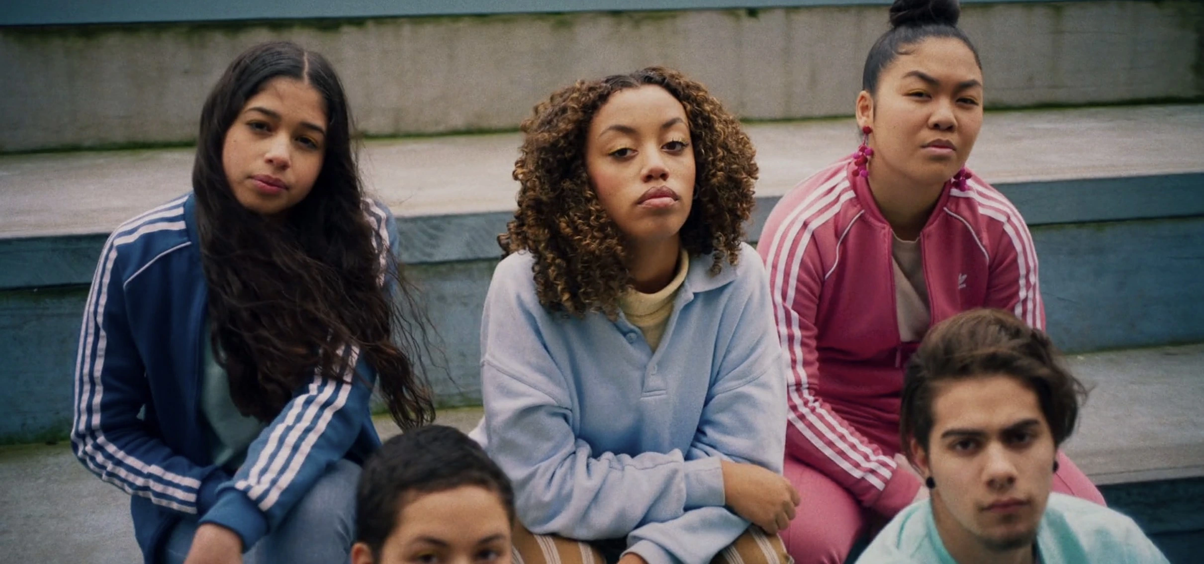A group of five individuals in activewear sit on concrete stairs, with disdained expressions on their faces. Mikki Sindhunata