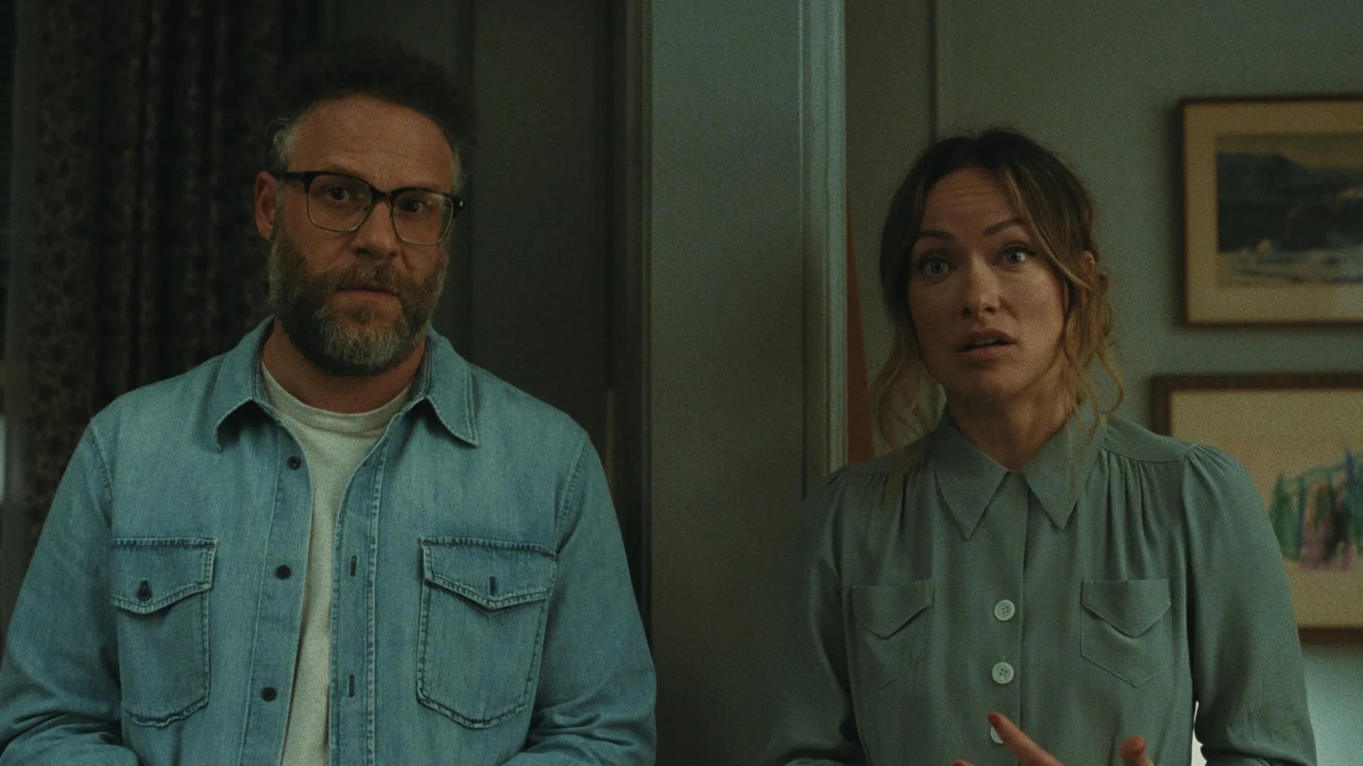 Olivia Wilde and Seth Rogen as a married couple in A24's The Invite, standing in a home interior