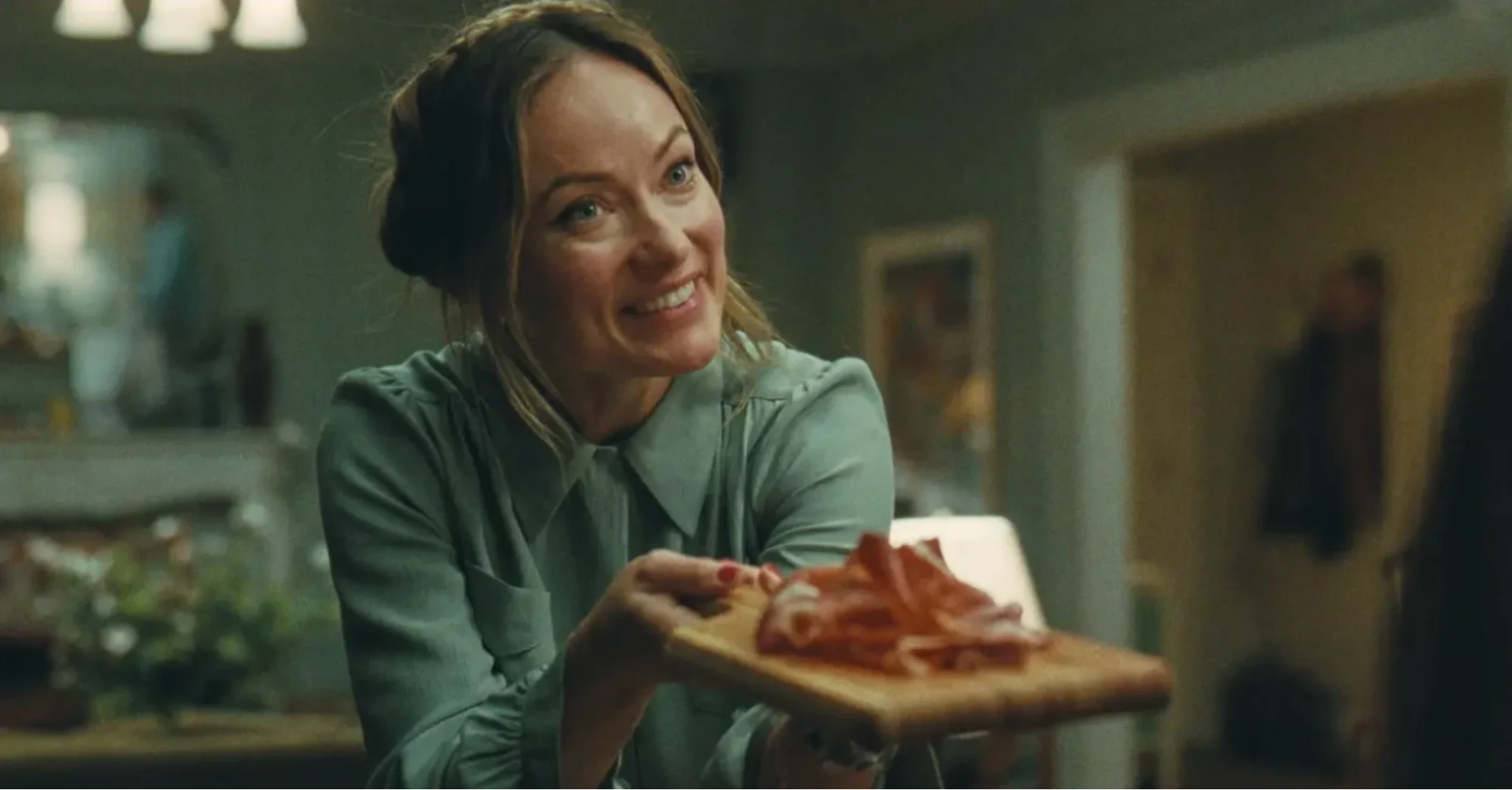 Olivia Wilde as Angela offering a wooden board of Jamon in A24 film The Invite